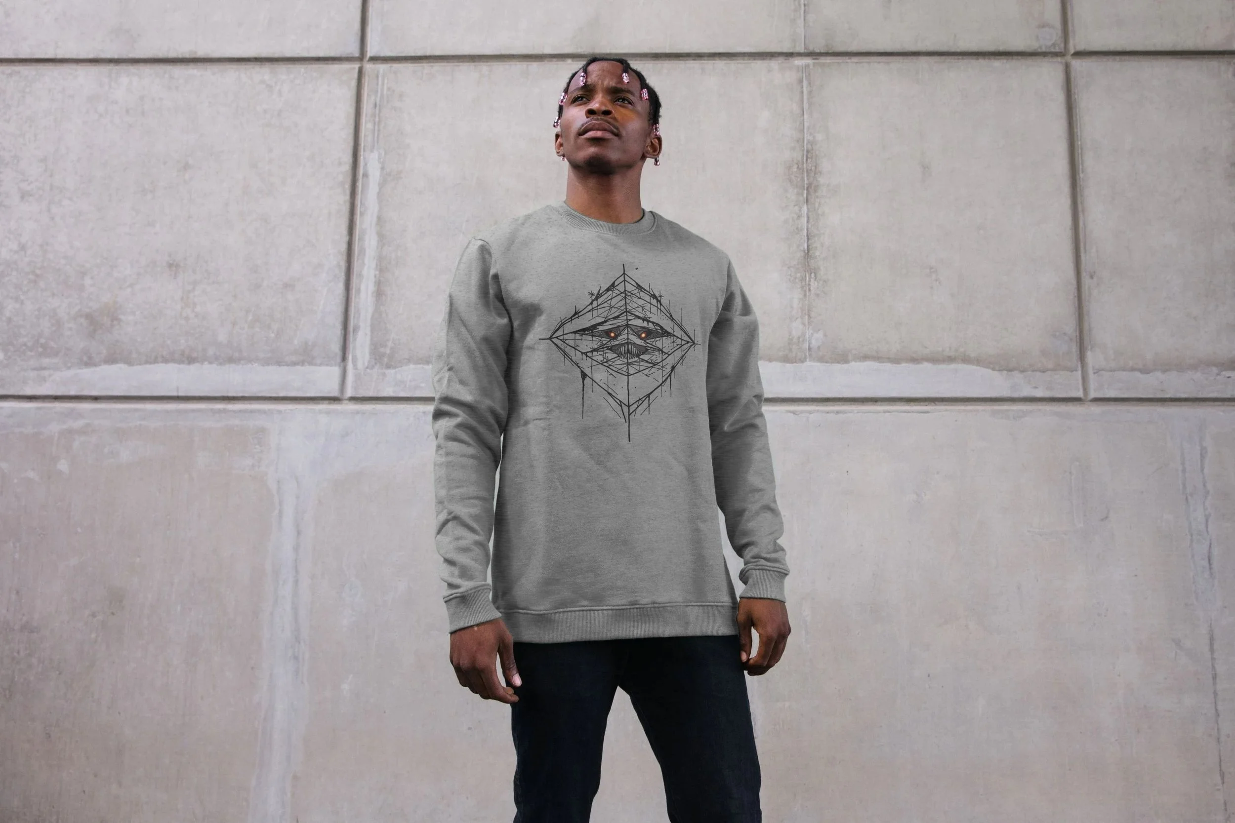 Model wearing the grey Raptor organic cotton sweatshirt by Mongrel Logic, featuring a geometric black line-art entity with glowing orange eyes.