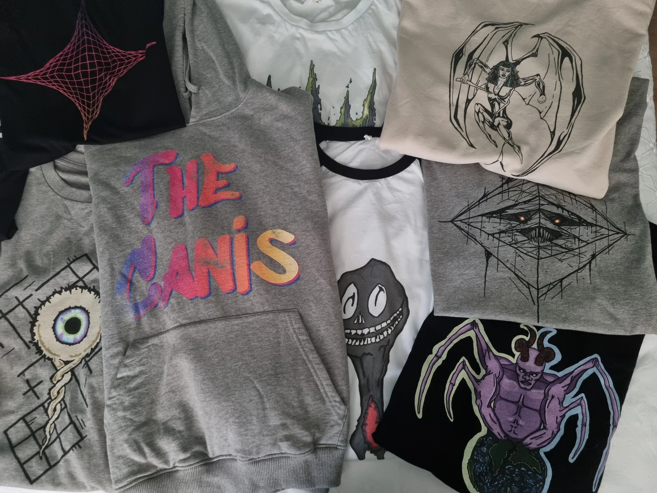 Flat-lay collection of Mongrel Logic organic cotton garments featuring Logic, Raptor, Sun Eater and The Canis artwork in black, grey and white.