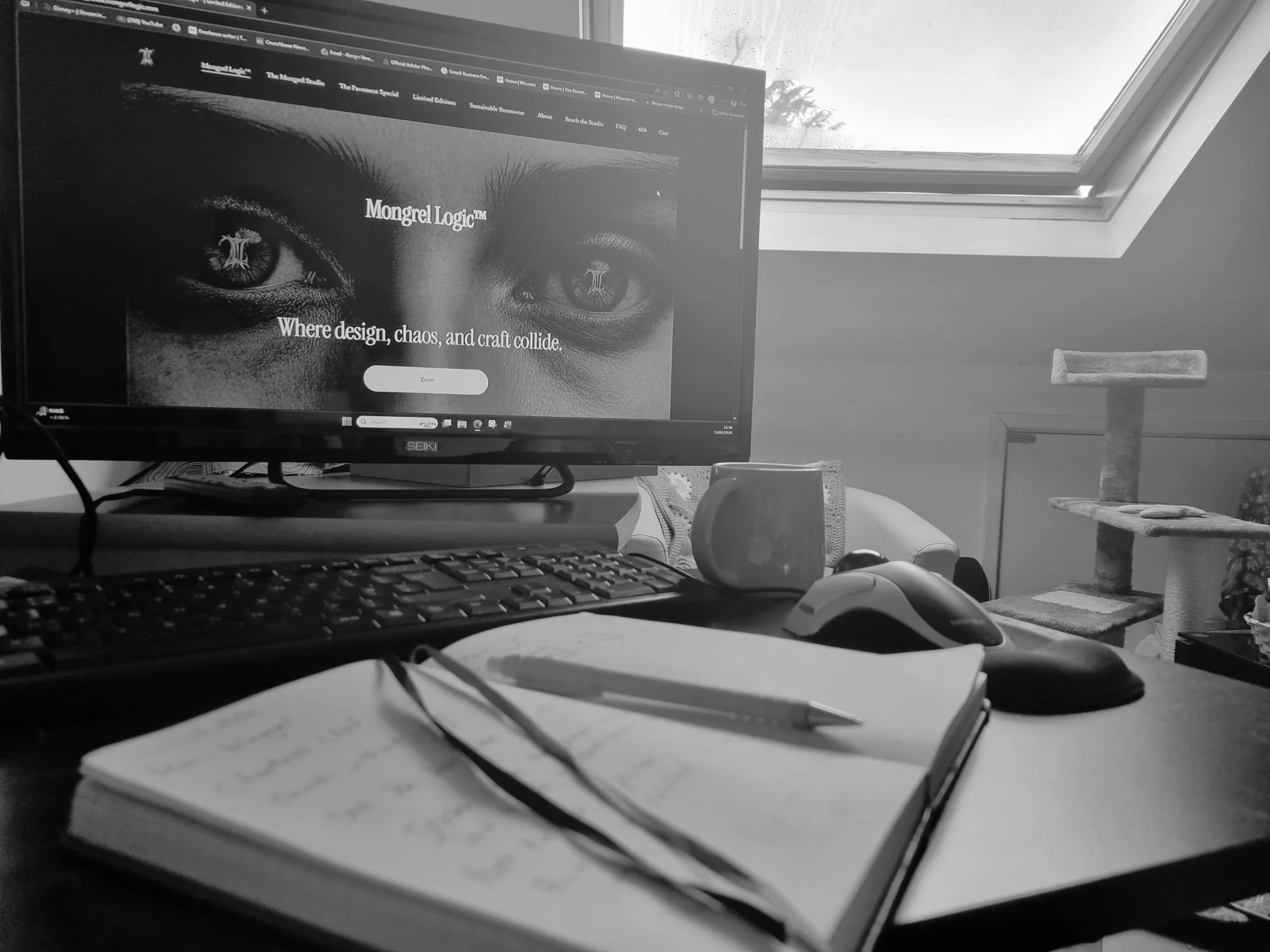 Black and white photo of a studio desk with notebook, keyboard, and Mongrel Logic website open on screen.