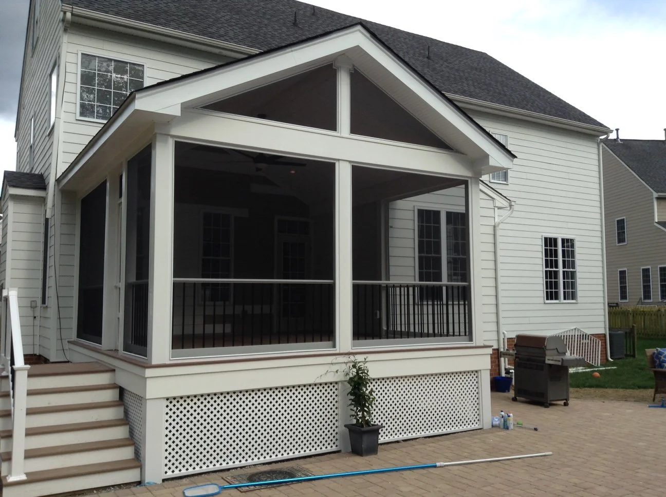Backyard view of a house with a screened-in porch, outdoor furniture, barbecue grill, and a paved patio area.
