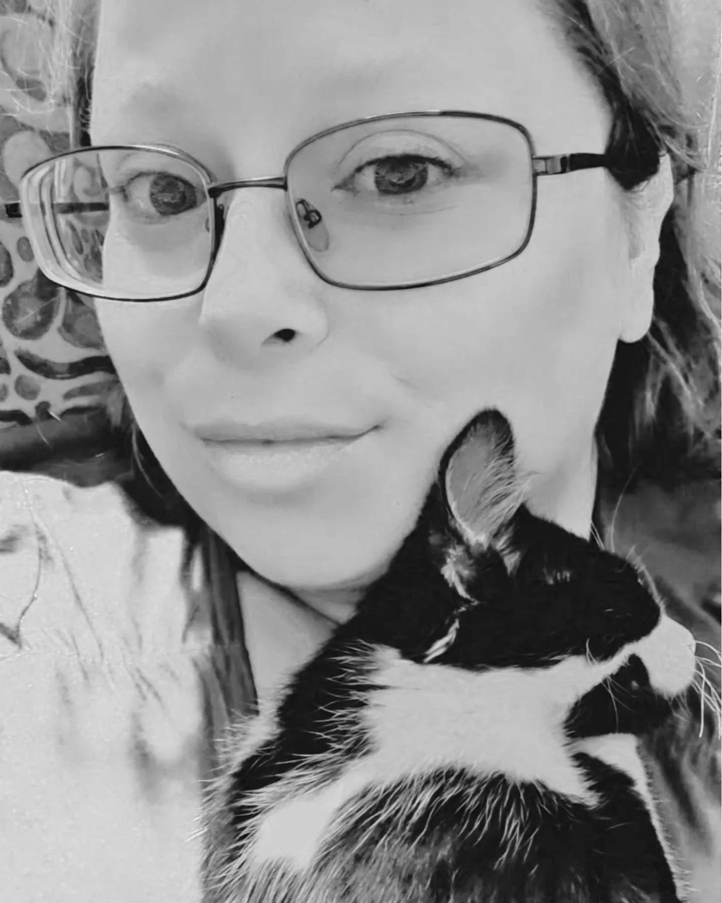 A woman with glasses holding a black and white kitten close to her face.