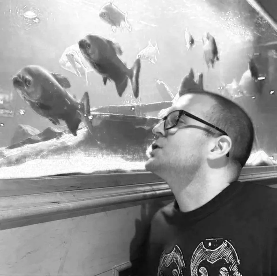A man with glasses resting his head against an aquarium glass containing several fish.