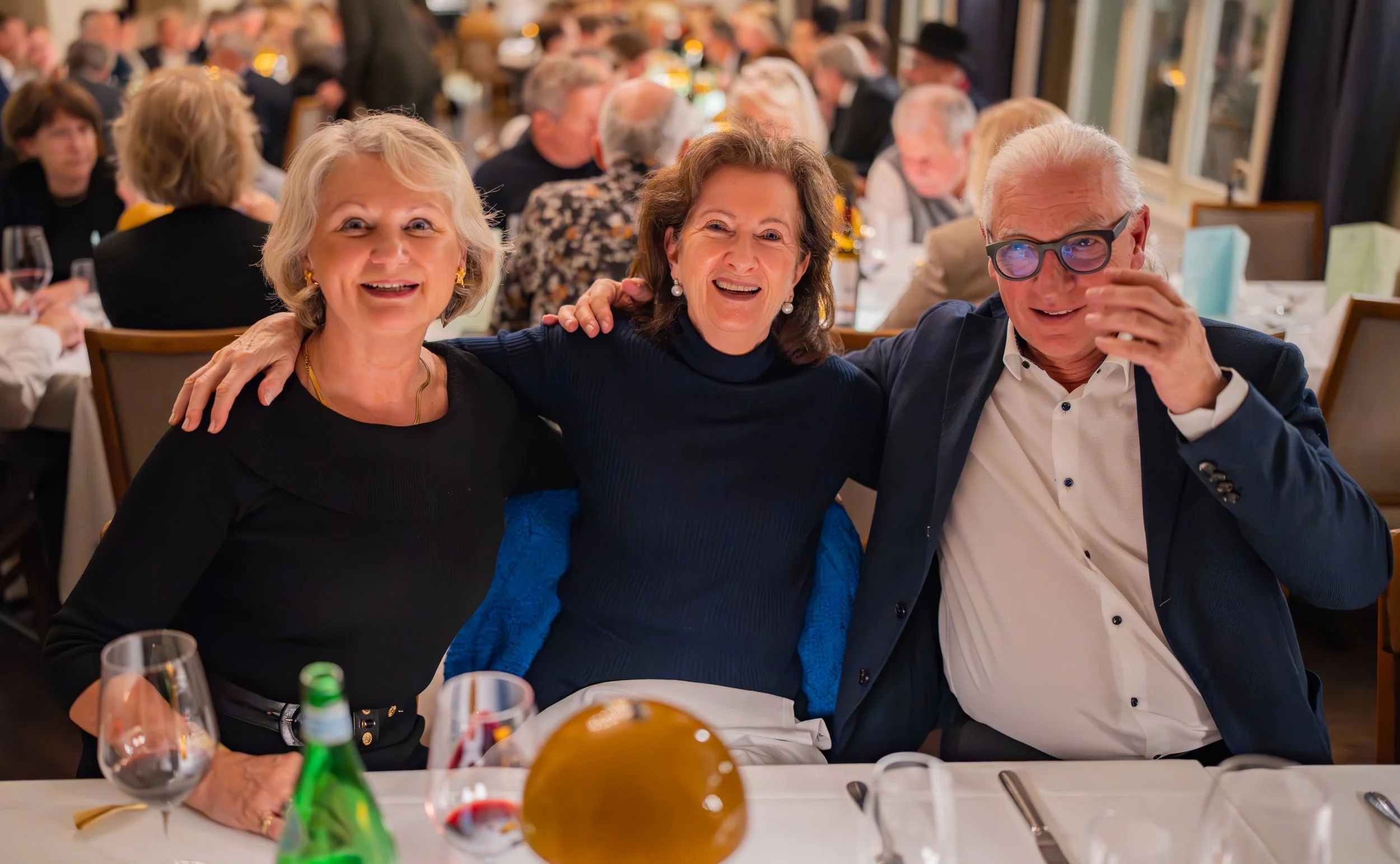 Drei lachende ältere Personen sitzen zusammen an einem Esstisch bei einer Feier im Restaurant