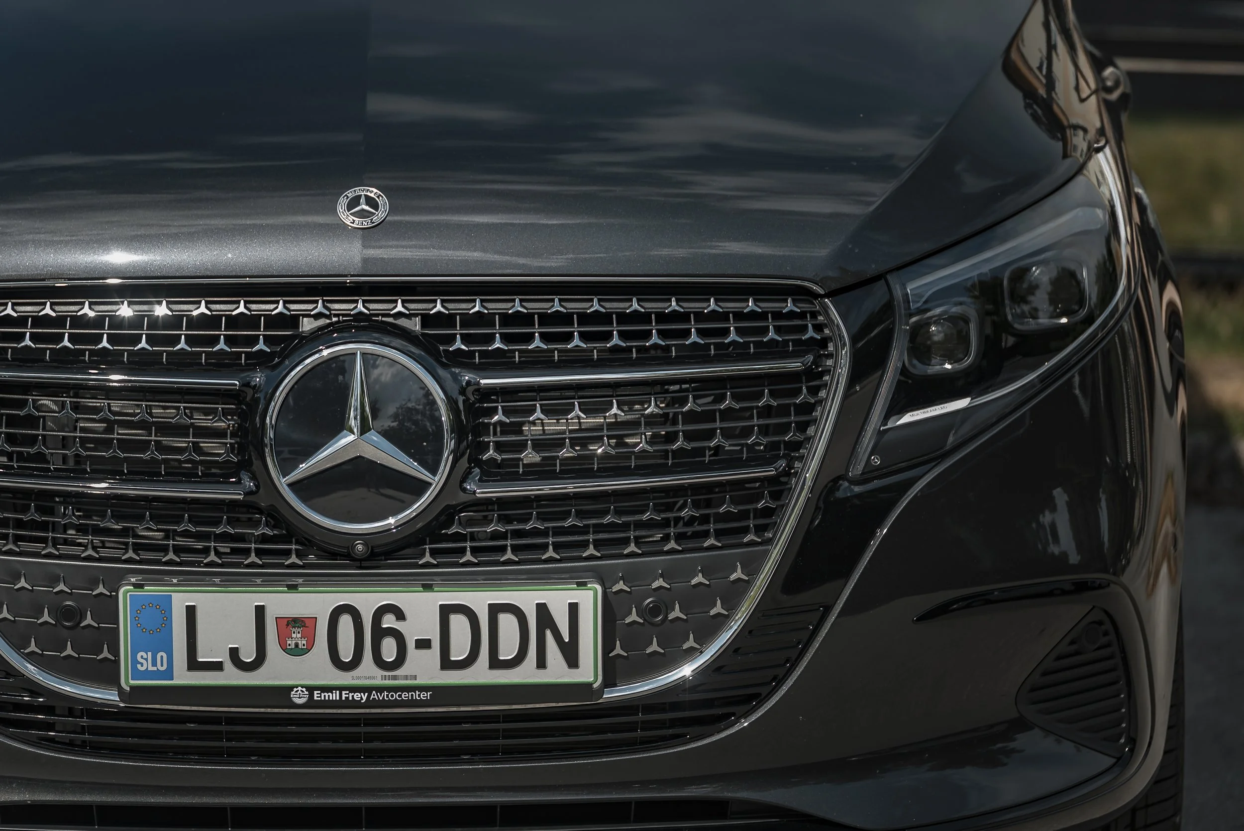 Close-up of a black Mercedes-Benz van, including grille with the Mercedes logo, headlights, and Slovenian license plate reading 'LJ 06-DDN'.