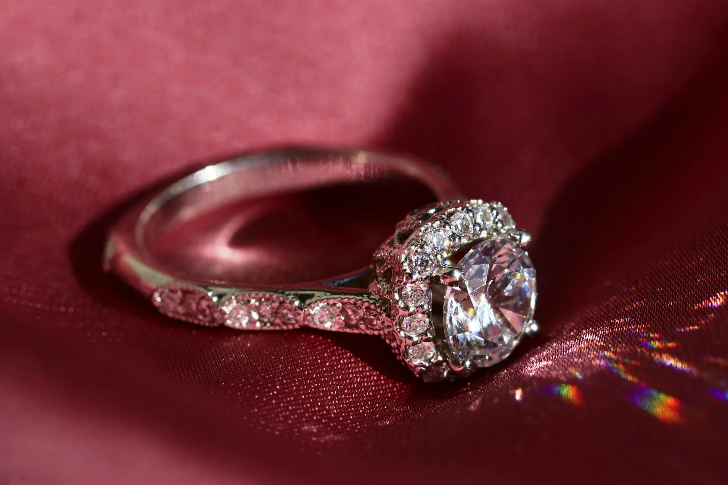 Een diamanten ring met een groot centrale steen en kleinere diamanten rondom, op een glanzende roze zijden stof.