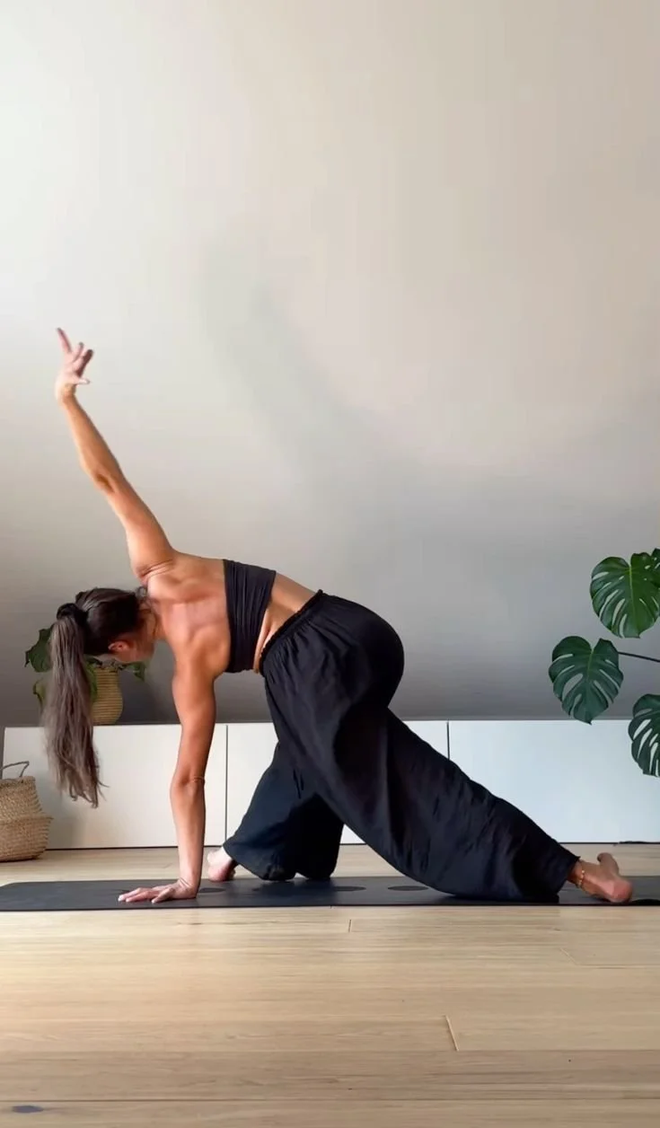 Femme faisant une pose de yoga dans une pièce avec plantes vertes.