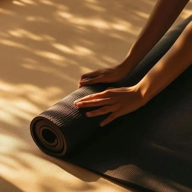 Personnes déroulant un tapis de yoga en position assise dans une pièce ensoleillée.