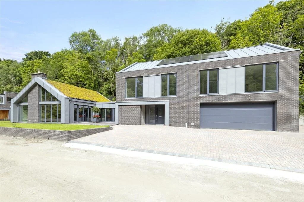 Modern two-story brick house with large windows and a garage, surrounded by trees