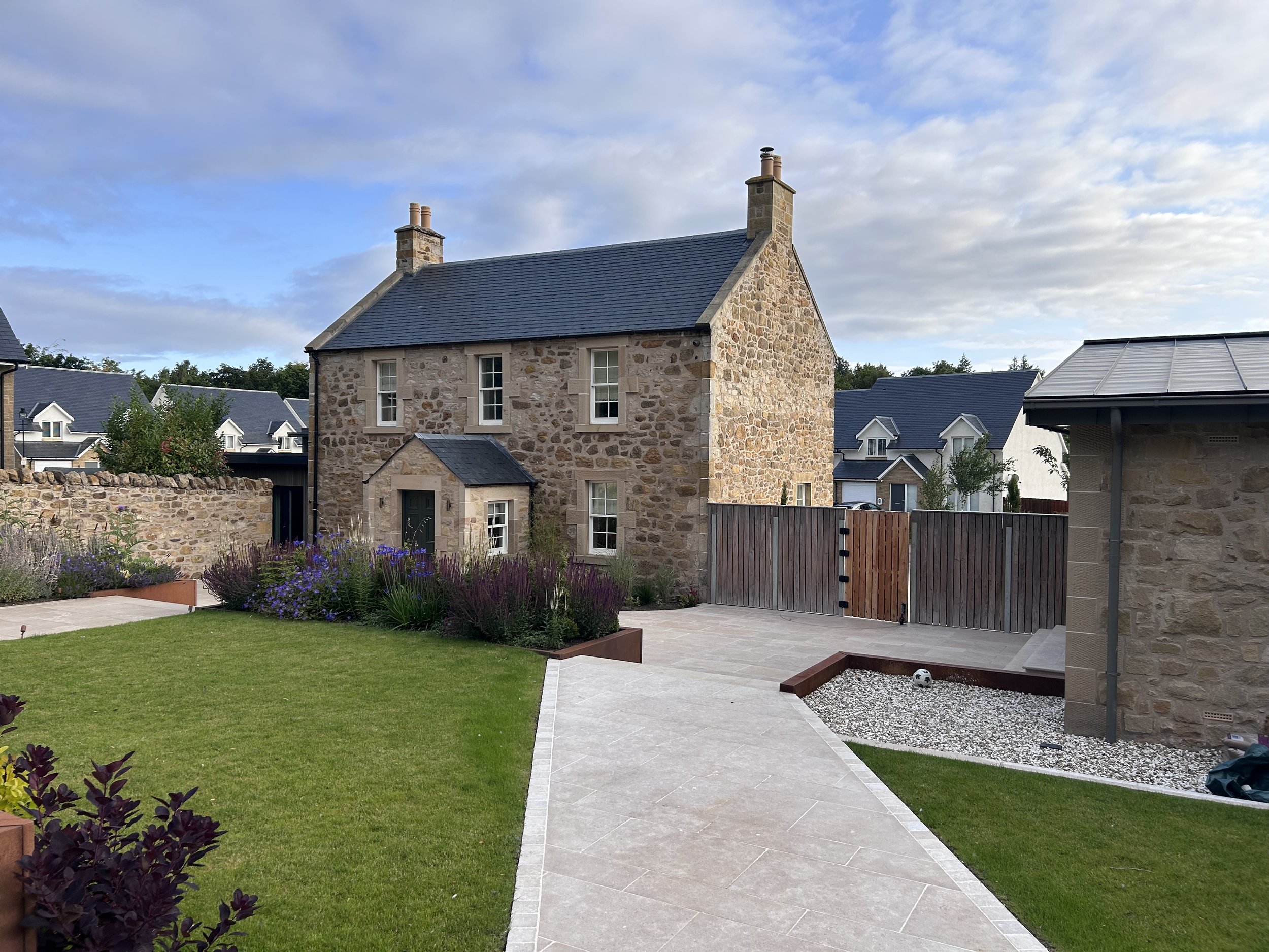 A stone house with a garden and pathway in a residential neighborhood.