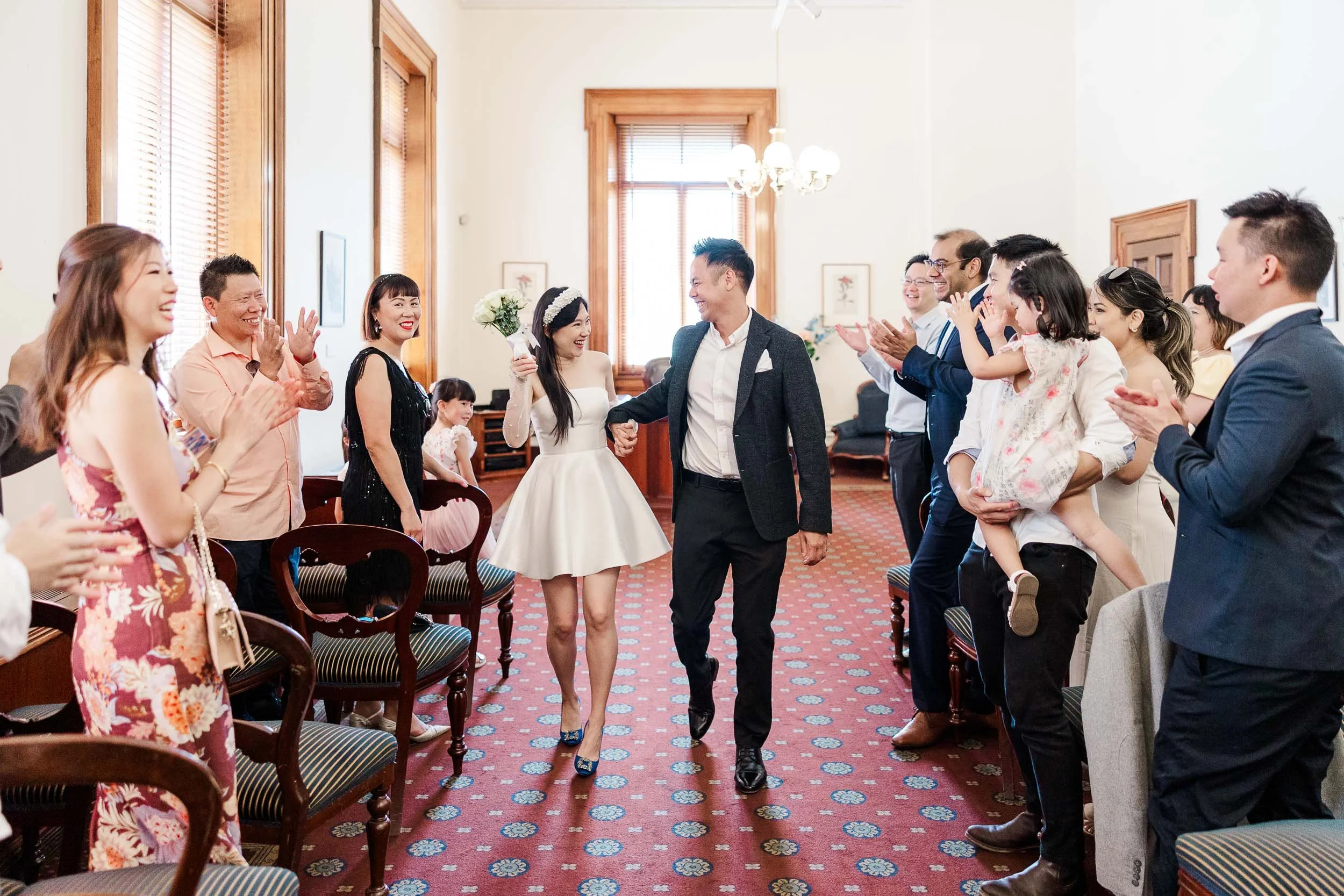 Melbourne civil wedding Old Treasury Building ceremony with newlyweds walking out smiling as guests applaud indoors.