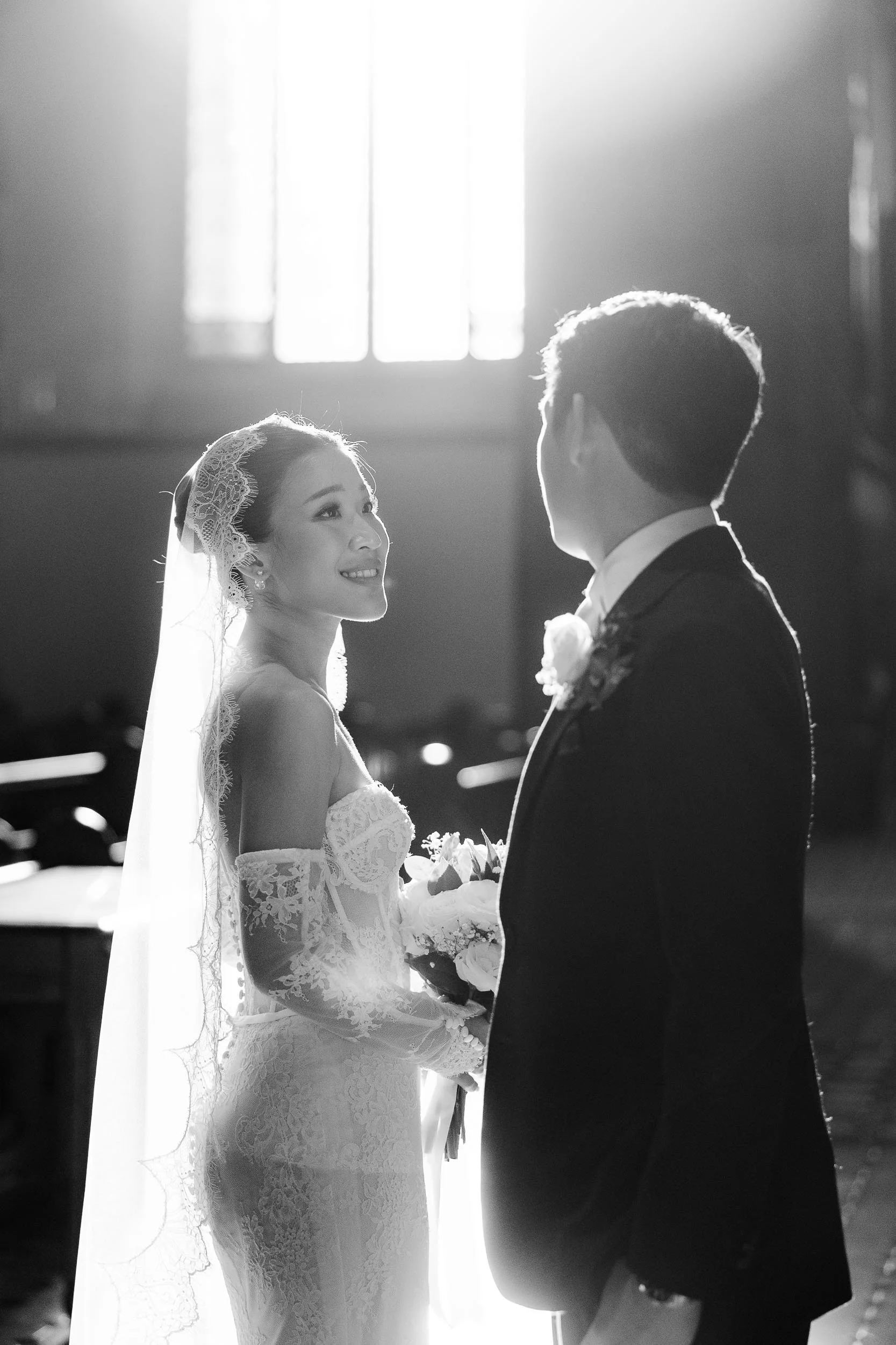 Black and white Melbourne wedding photography of a bride and groom in st patrick's church, backlit by a glowing window during portraits.