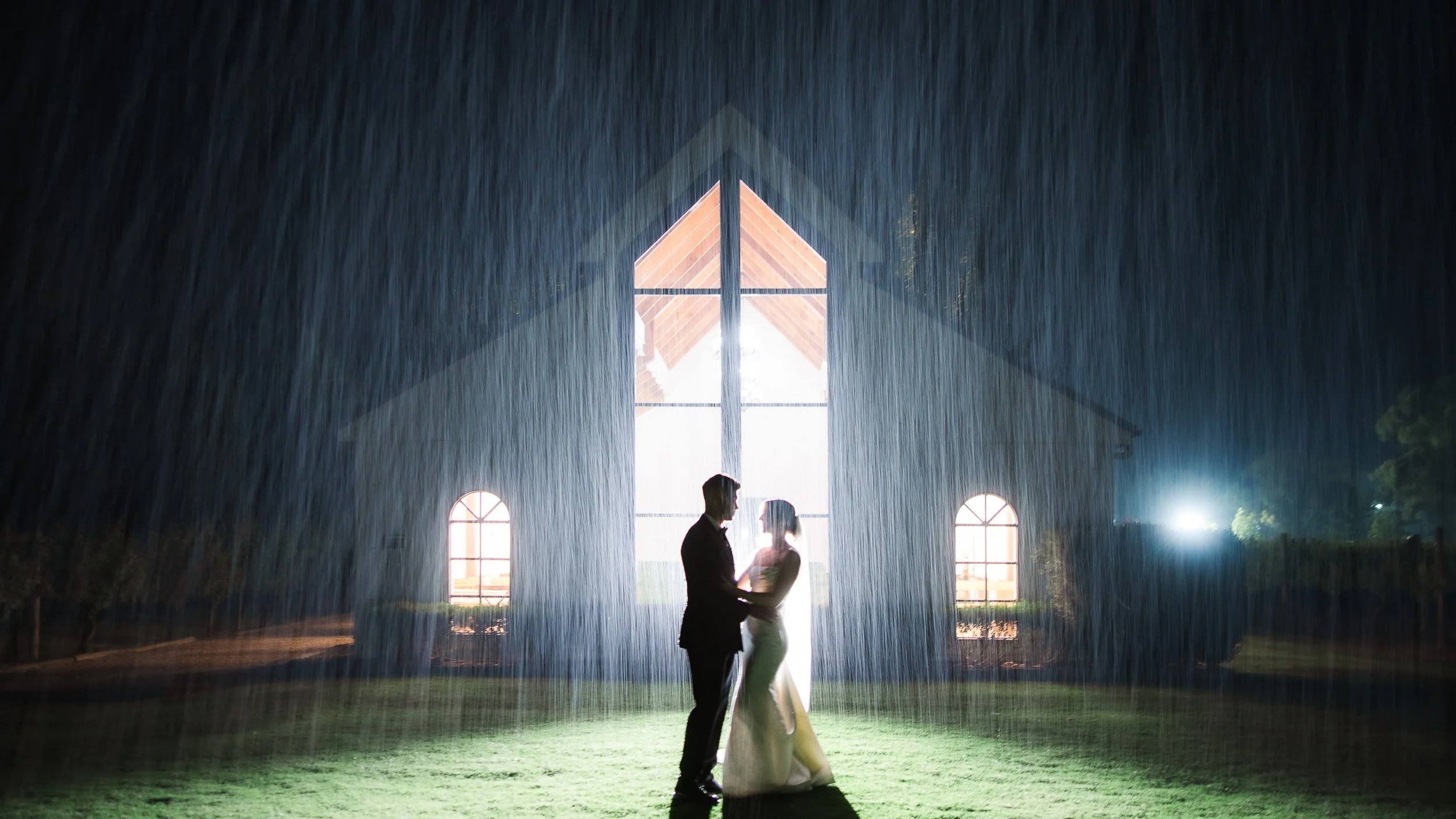 Bride and groom photographed in heavy rain at night, showing how an experienced Melbourne wedding photographer works in difficult weather.