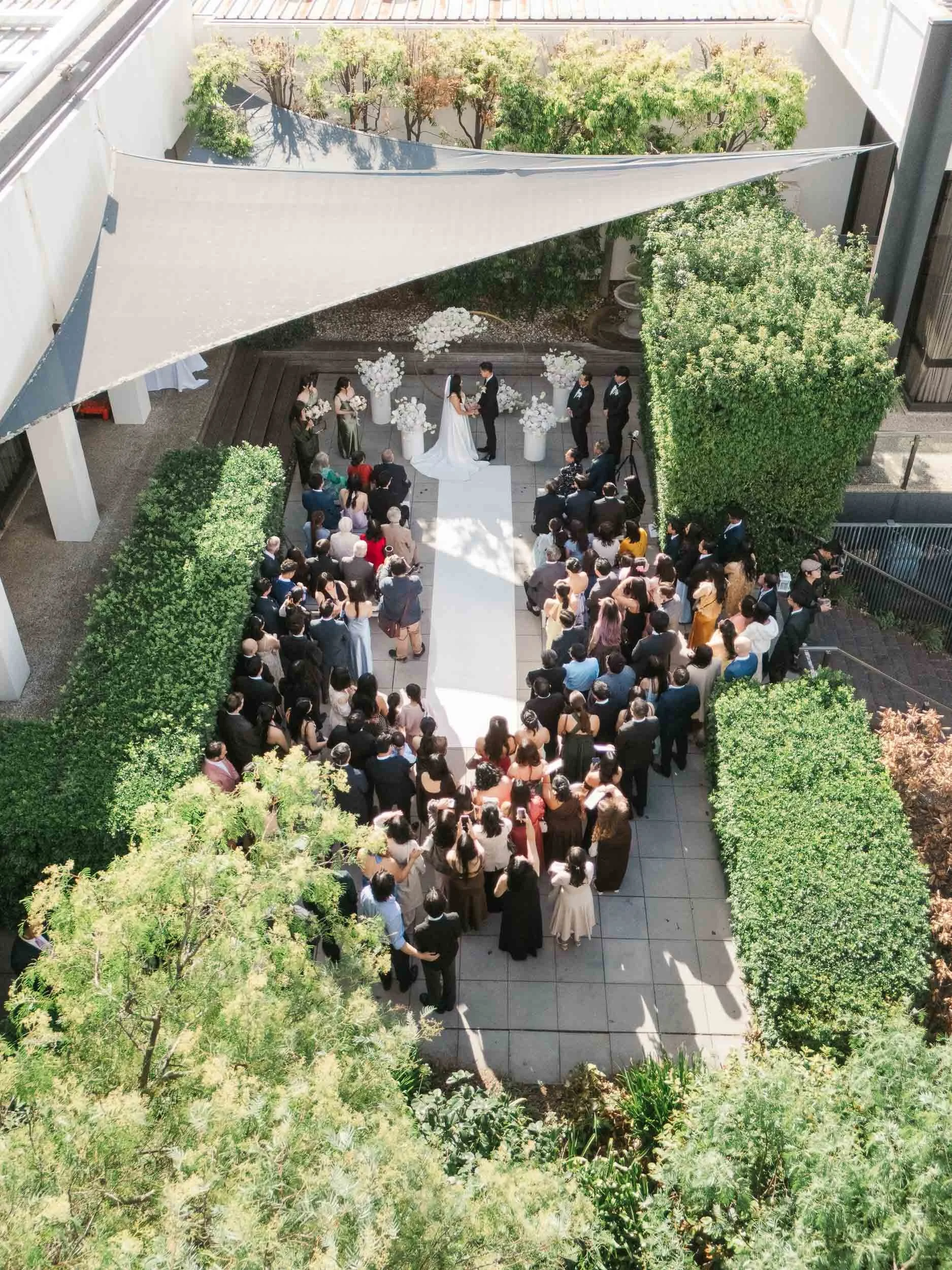 Melbourne wedding photography of an outdoor ceremony from above, with guests gathered around the couple in a modern courtyard of Leonda By The Yarra