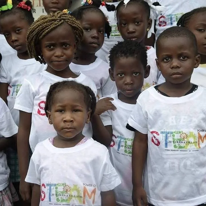 A group of young children in Liberia wearing white ITAVAC Power of STEAM t-shirts.