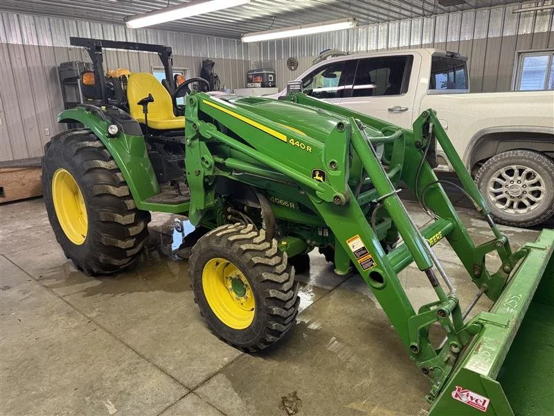 Green John Deere 440 R front loader tractor inside a garage with a silver pickup truck in the background.