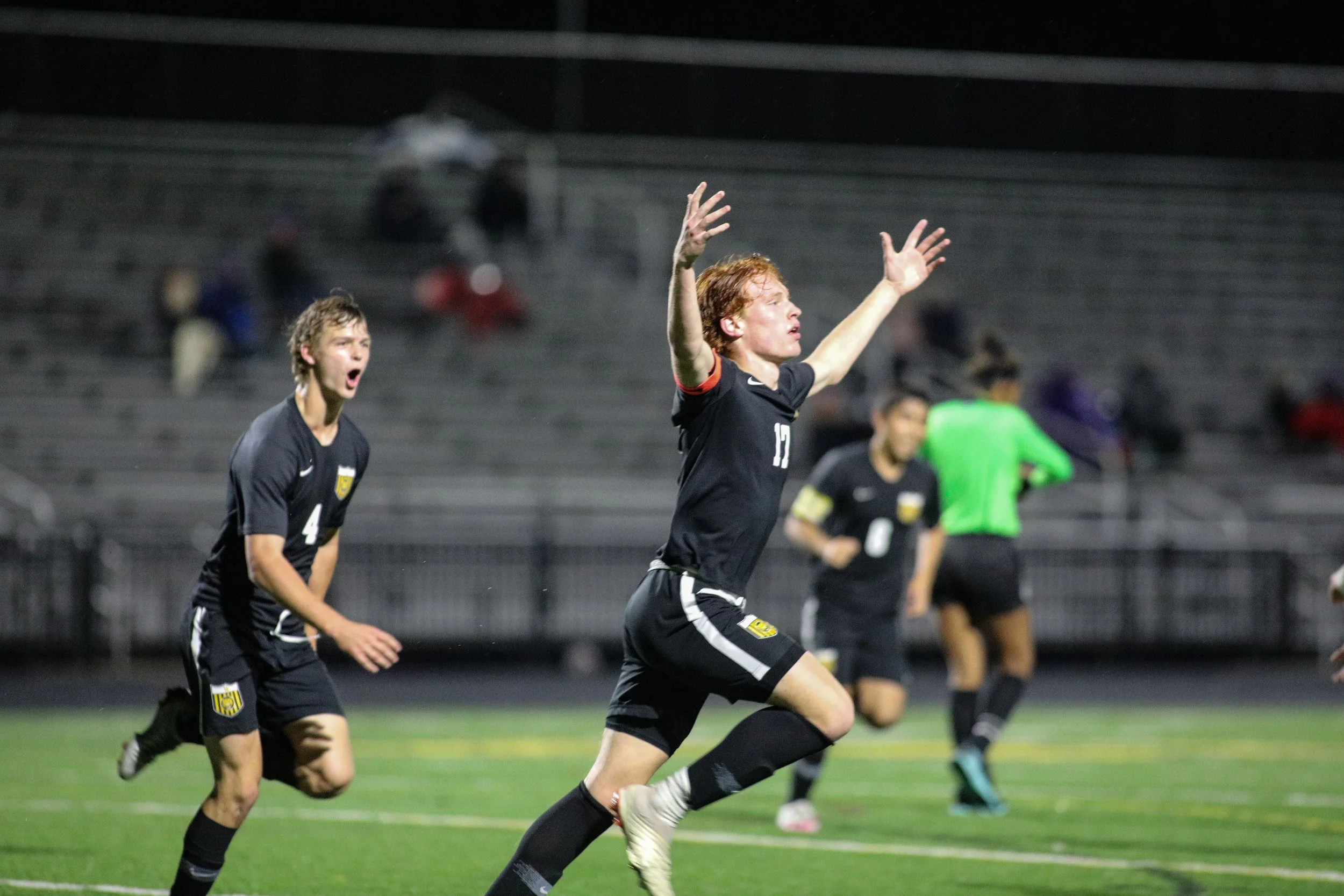 Soccer players celebrating on the field at night, with stands and spectators in the background
