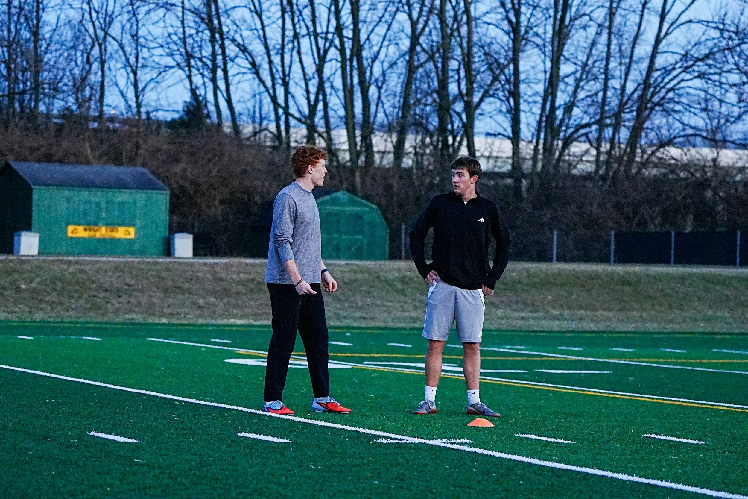 A soccer player with red hair running on a green field with a soccer ball.
