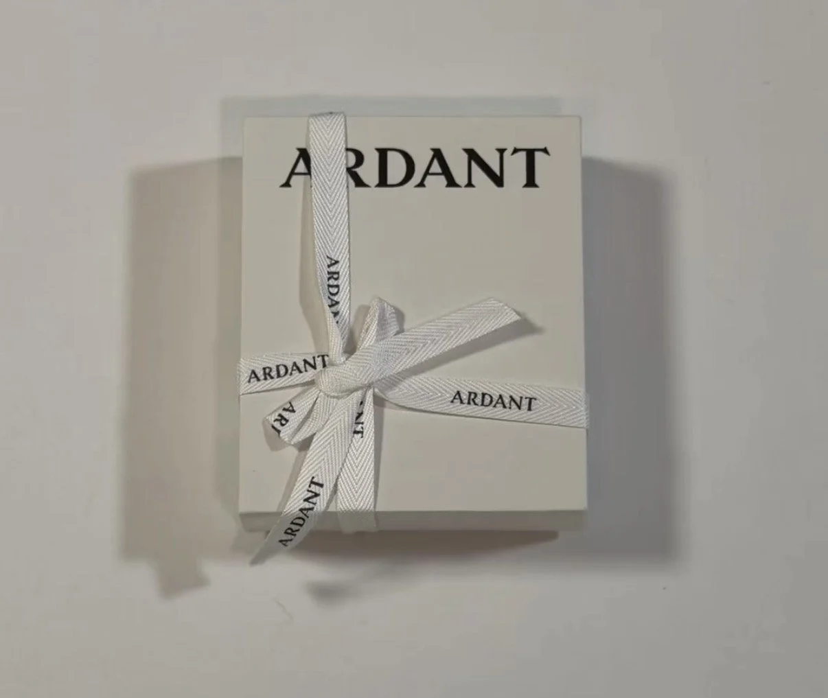 A white box with the word 'ARDANT' on it, tied with a white ribbon that has 'ARDANT' printed on it.