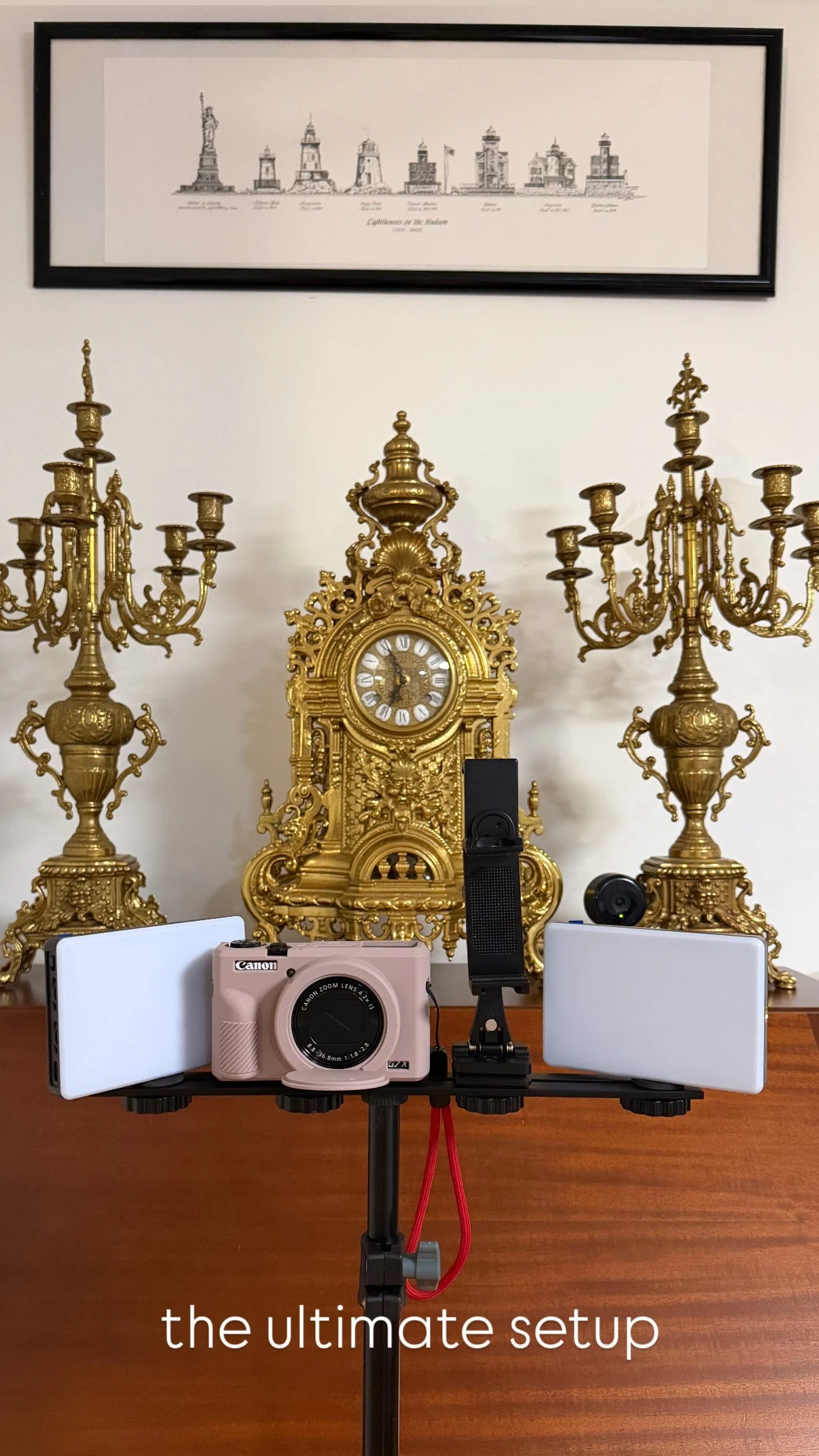 A photography setup with a smartphone on a tripod in front of an ornate gold clock and candelabra, with framed artwork of landmarks on the wall behind. The text overlay says 'the ultimate setup'.
