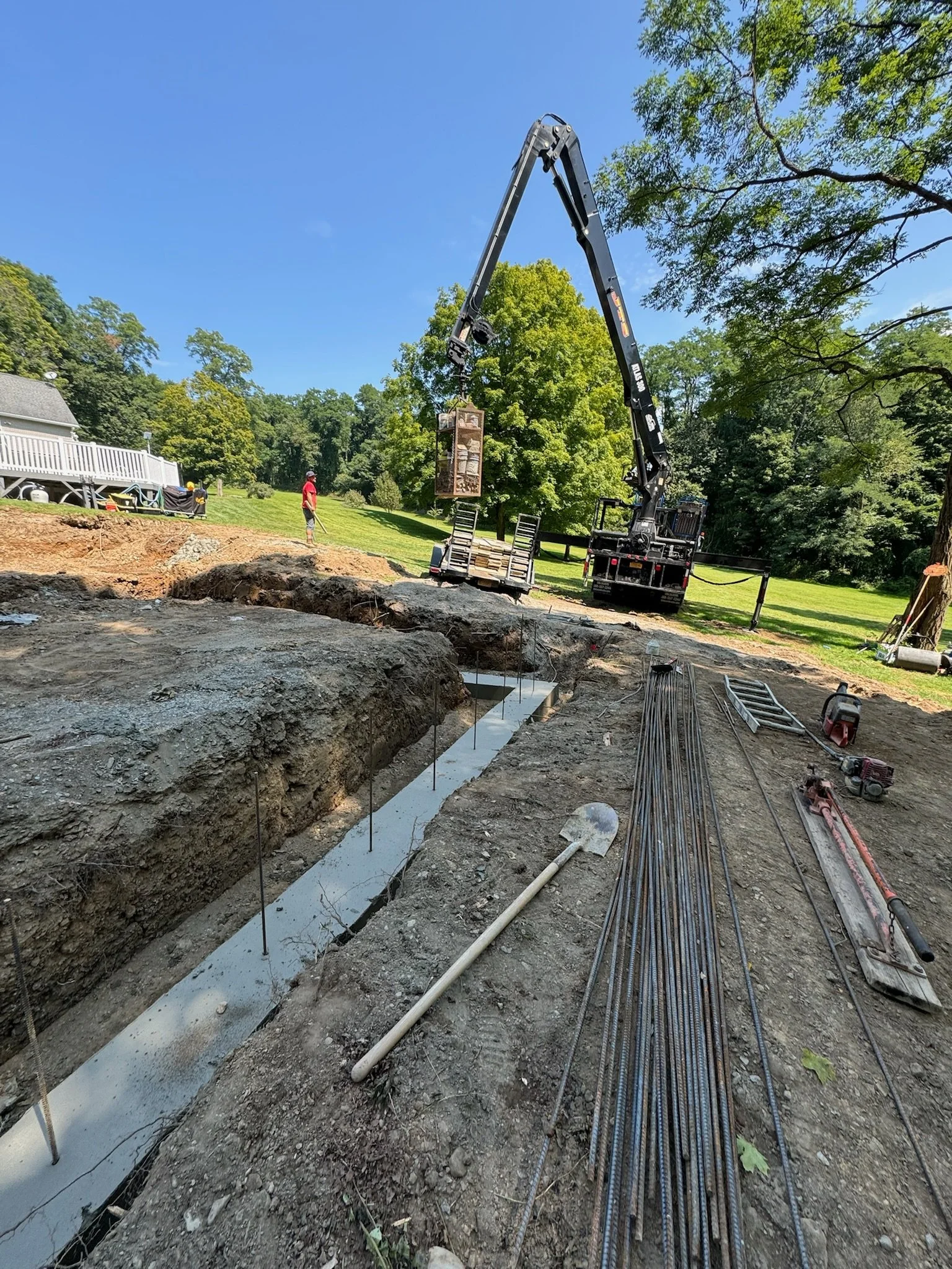 Construction site with a large crane pouring concrete into foundation trenches, surrounded by tools and construction materials.