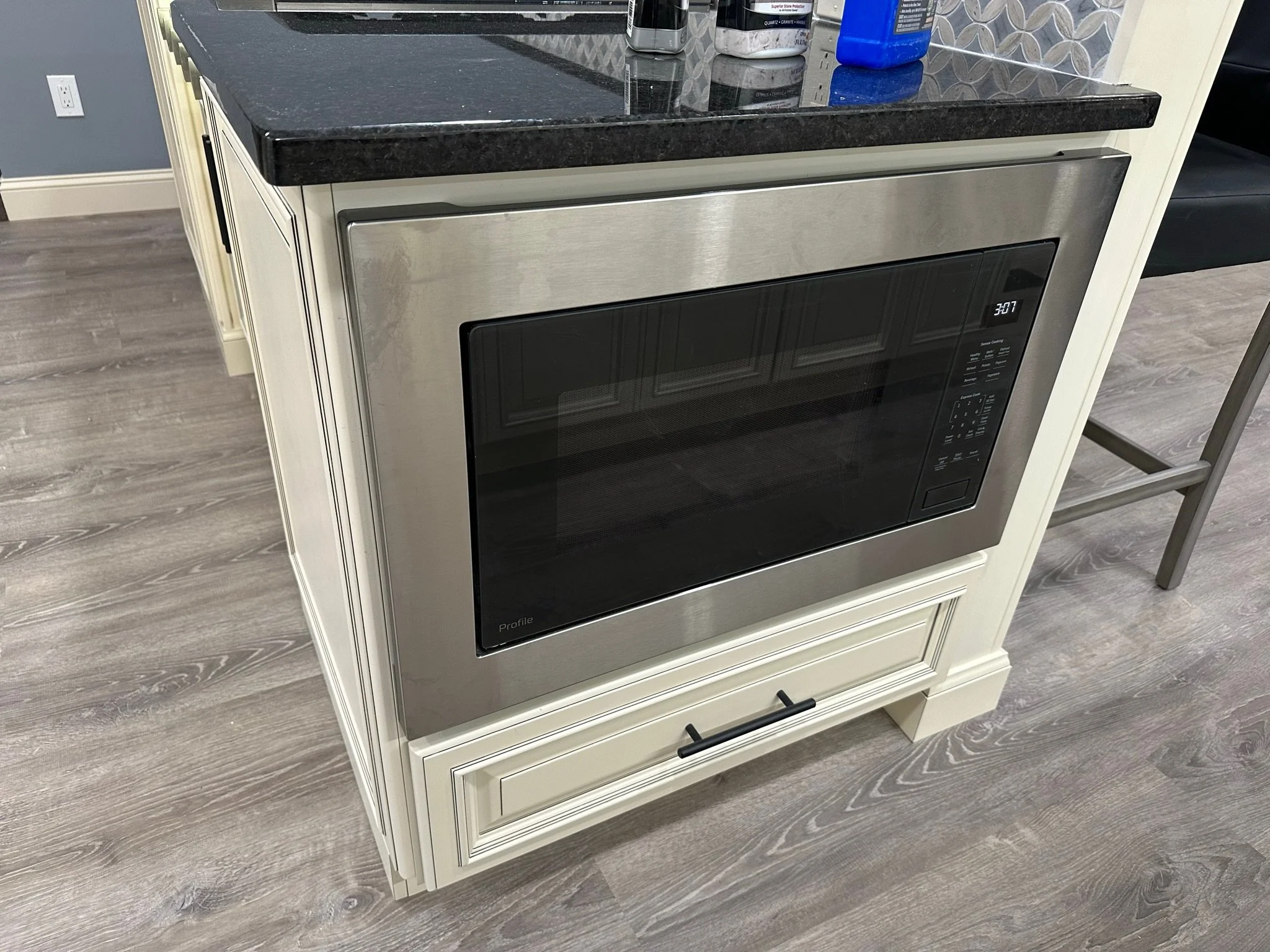 Stainless steel microwave oven installed in a cream-colored kitchen cabinet with a black countertop.