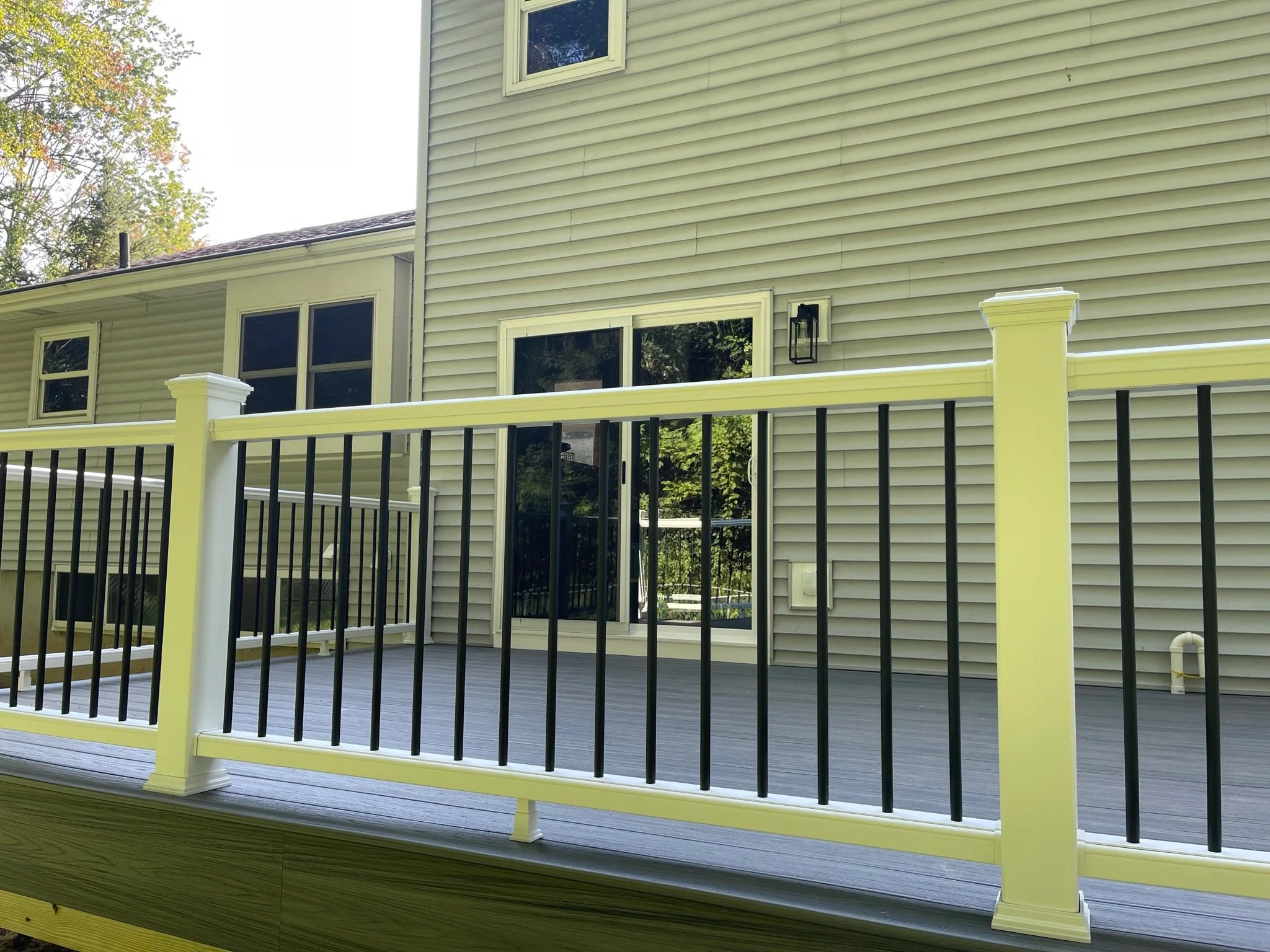 Backyard deck with black and white railing attached to a beige house with vinyl siding, windows, and a door.