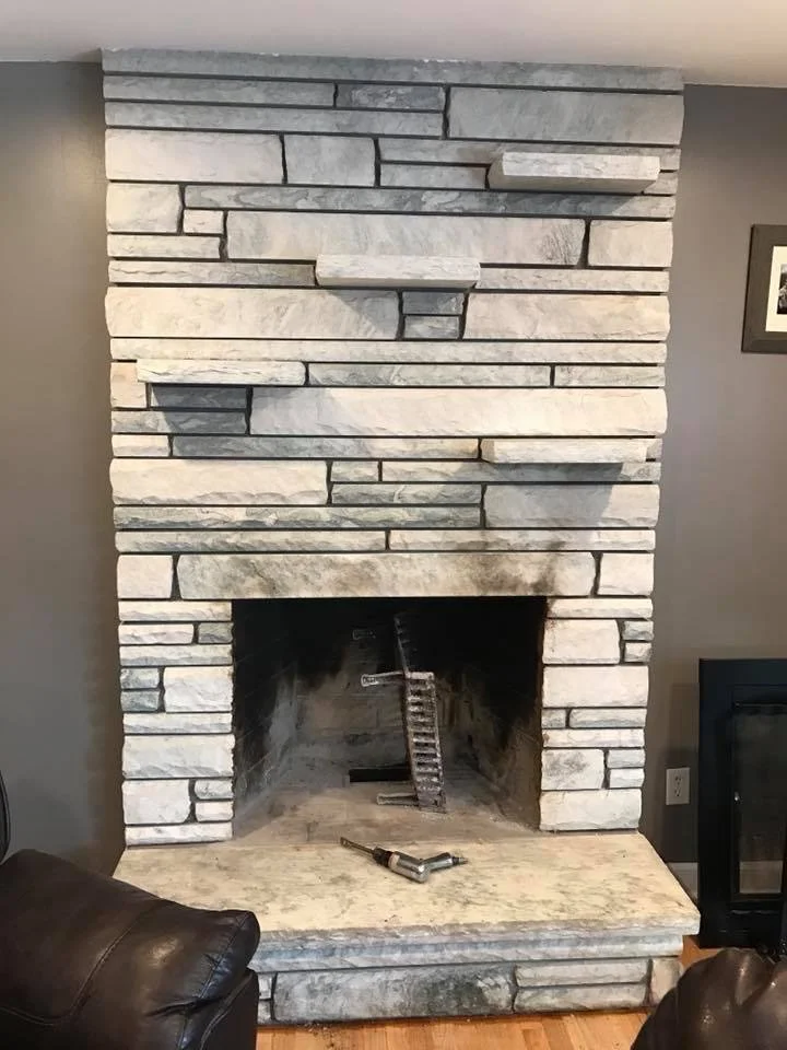 A stone fireplace in a living room with a brick hearth and a partially assembled chimney. Tools are placed inside the fireplace.