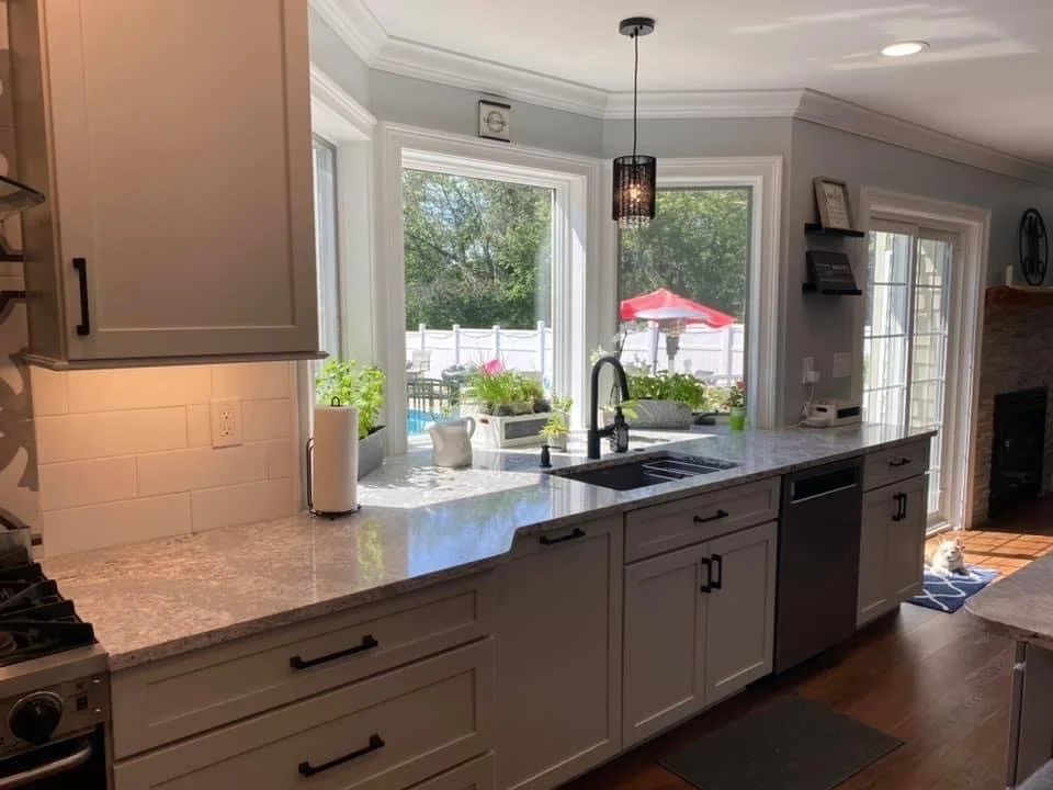 Modern kitchen with white cabinets, granite countertops, and a large window above the sink showing an outdoor patio with a red umbrella.
