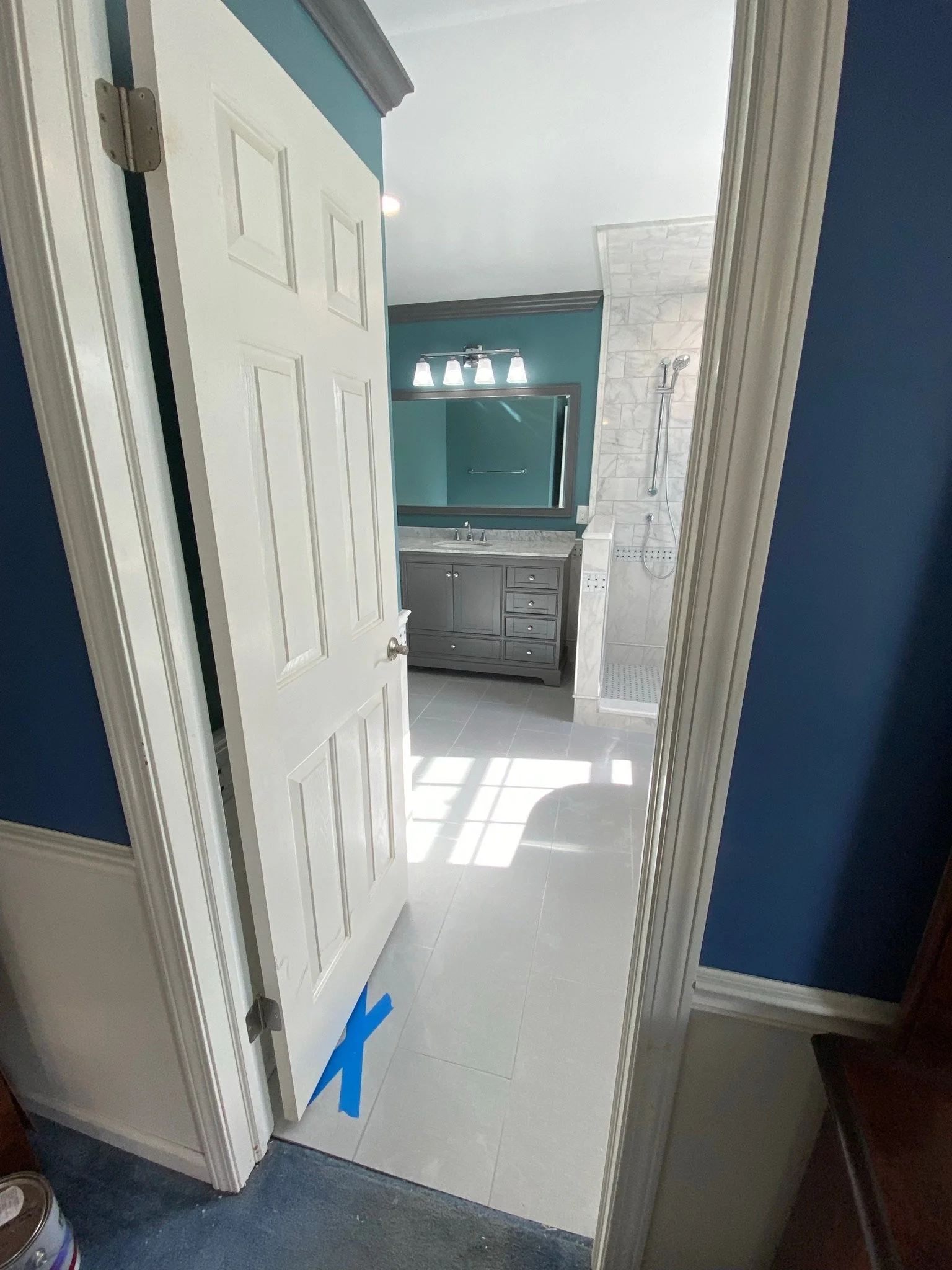 Bathroom with a door slightly open, showing a vanity with a mirror, sink, and gray cabinets, and a walk-in shower with gray tile walls and a handheld showerhead.