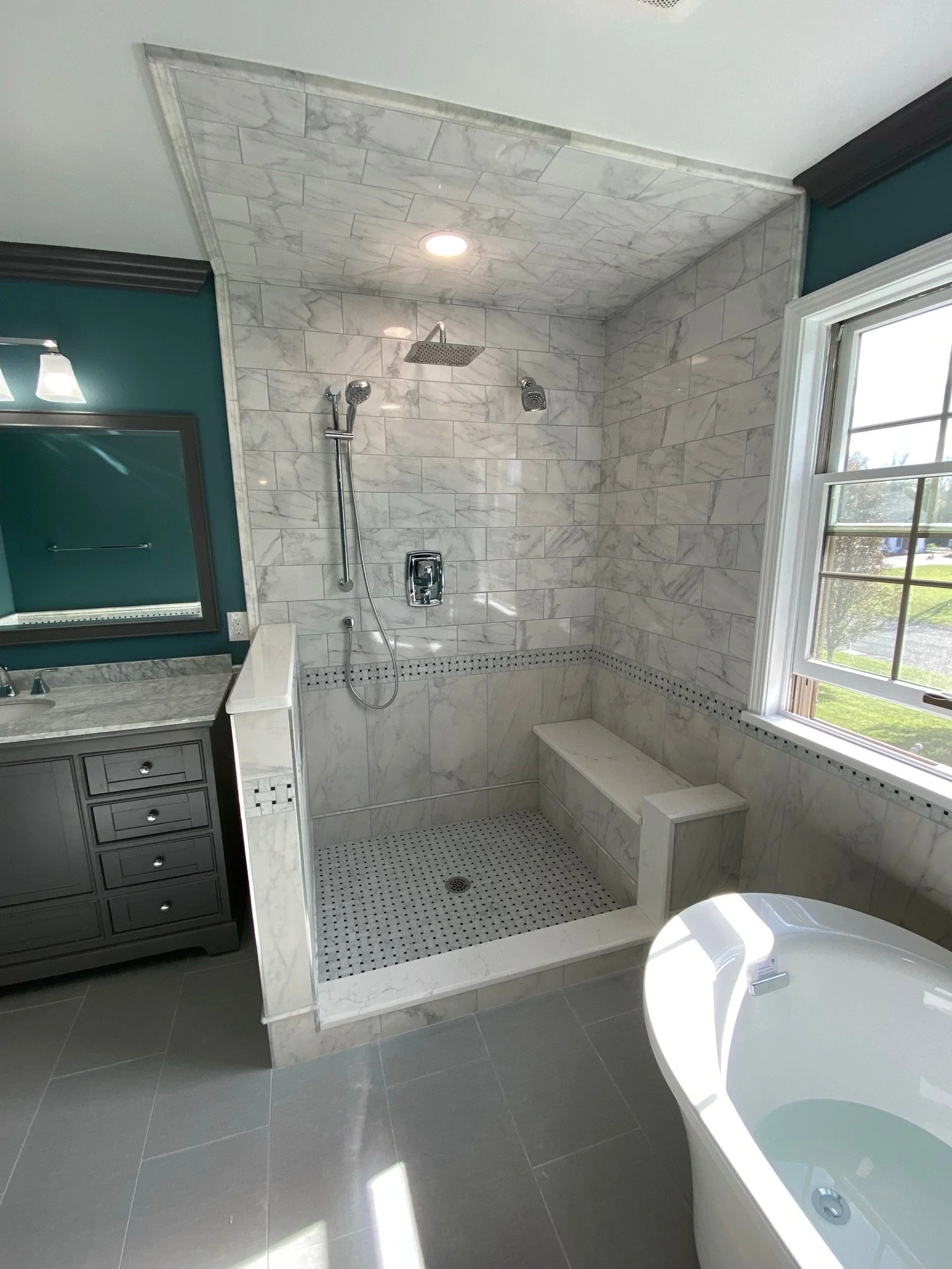 Marble shower with bench, stainless steel fixtures, and a window in a modern bathroom.