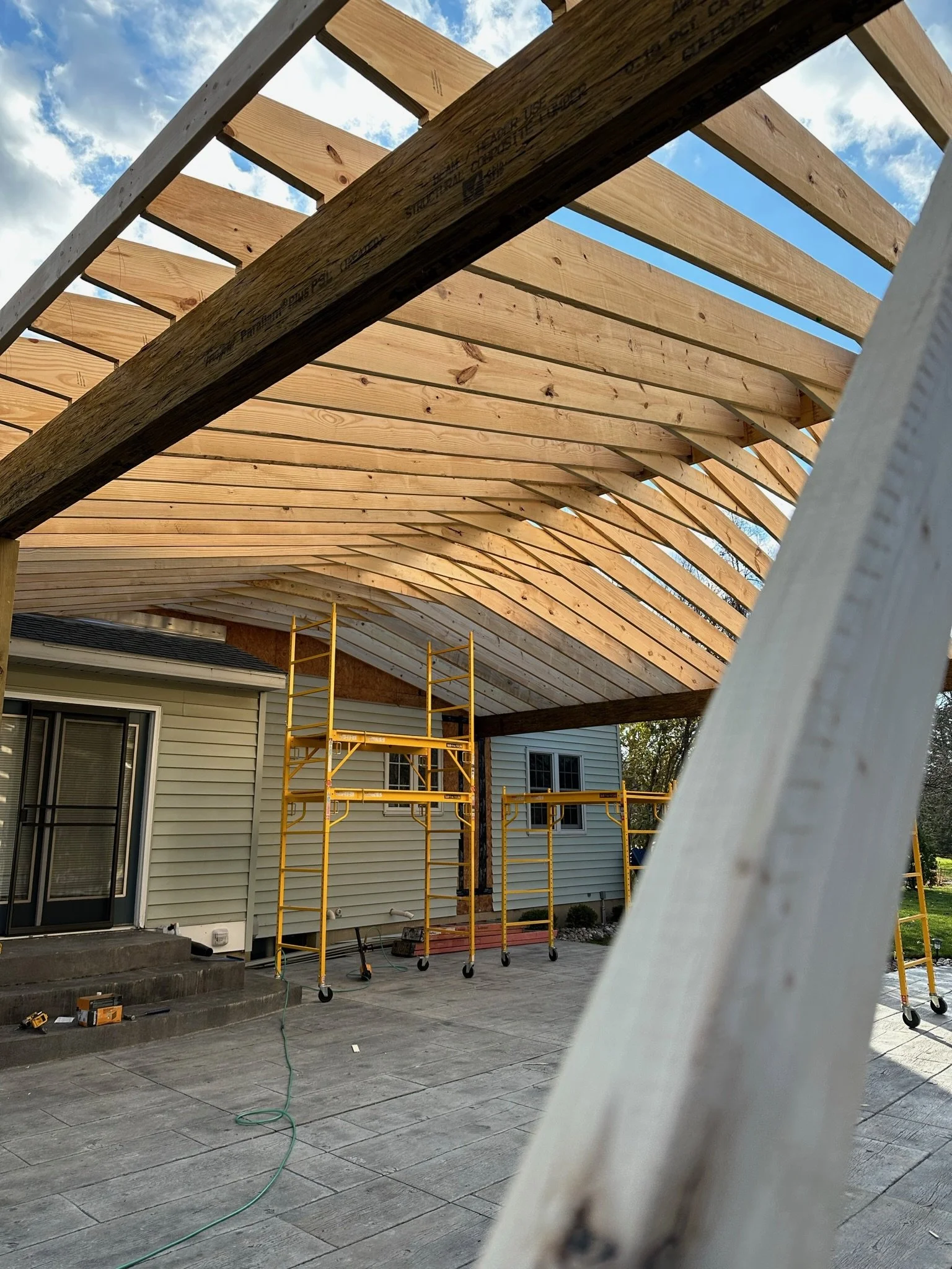 Construction of a new covered patio or addition at the back of a house with scaffolding and wooden beams for the roof framework.