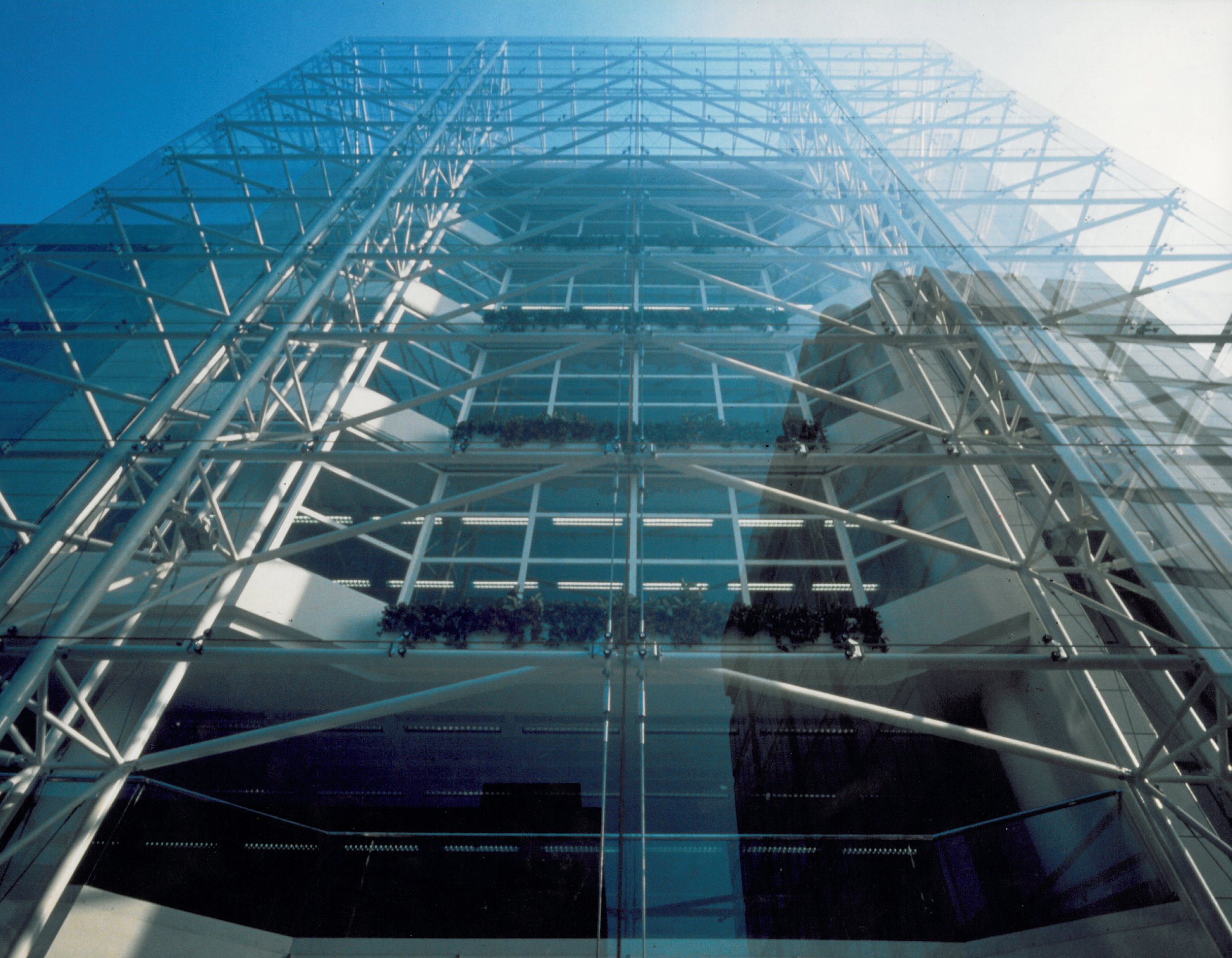 A tall modern glass building with a visible steel framework from below, looking upward.