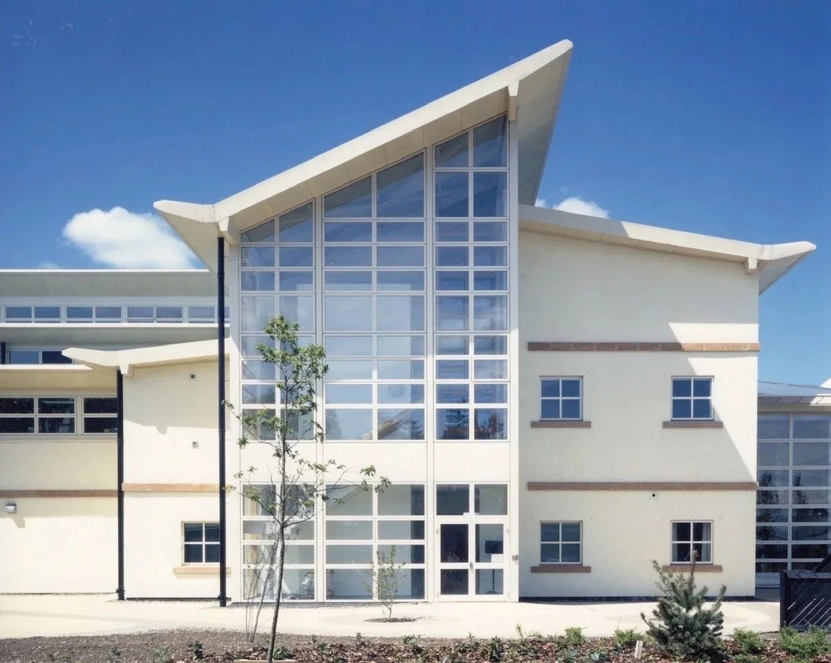 Modern building with large glass windows, sloped roof, and beige exterior walls under a blue sky.