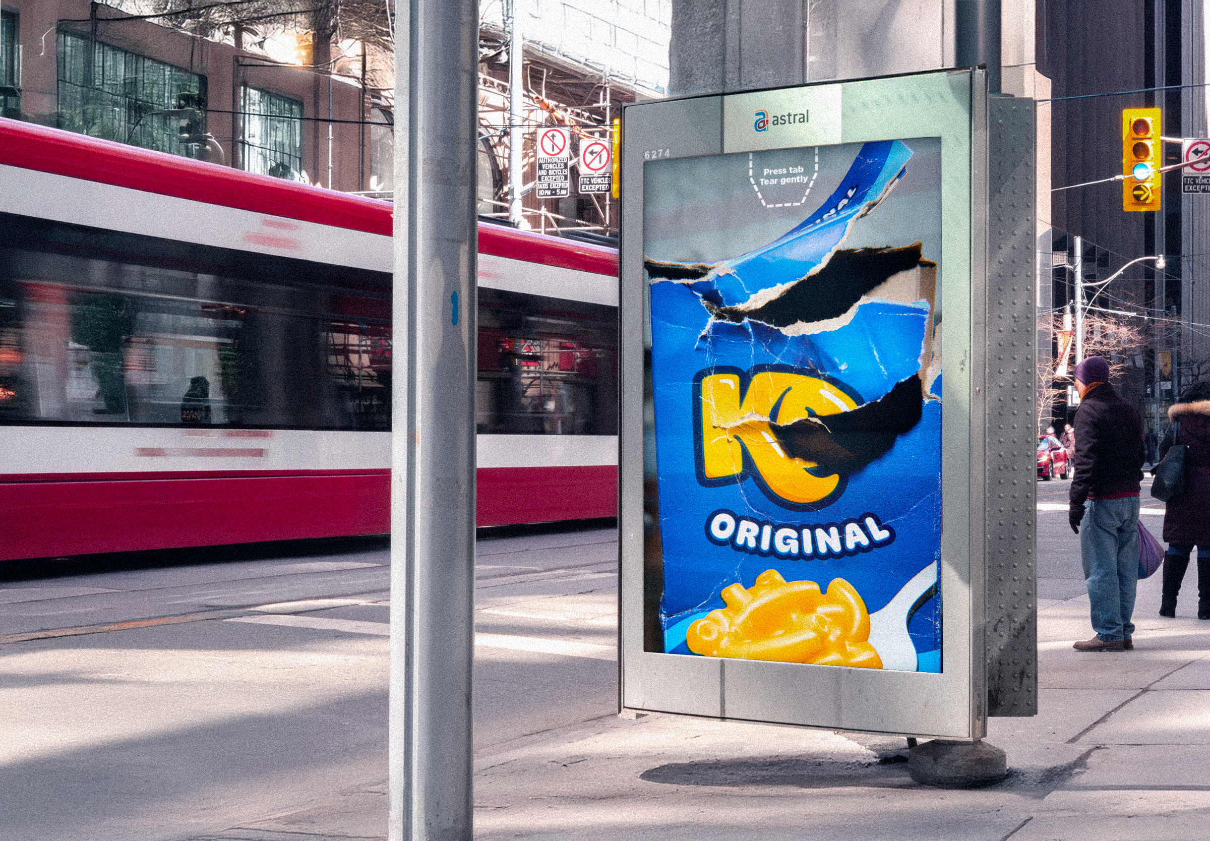 Une publicité sur un panneau à côté d'un arrêt de tramway montrant un paquet de chips Ruffles avec des déchirures visibles, dans une rue urbaine avec des piétons et un tram en mouvement.