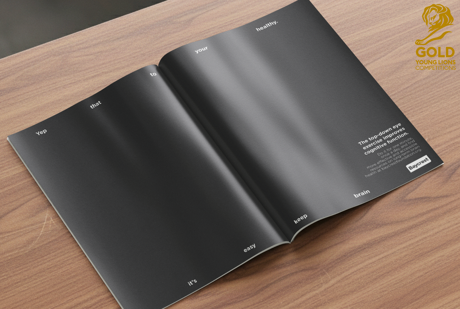 Livre ouvert avec texte blanc sur fond noir, contenant des mots en anglais comme "Yep," "that," "to," "your," "healthy," "brain," "keep," "easy," "it's," et un paragraphe sur l'amélioration de la fonction cognitive par l'exercice de l'œil supérieur droit, avec une référence à Bayercrest. Logo d'une lionne dorée avec l'inscription "GOLD YOUNG LIONS COMPETITIONS" en haut à droite.