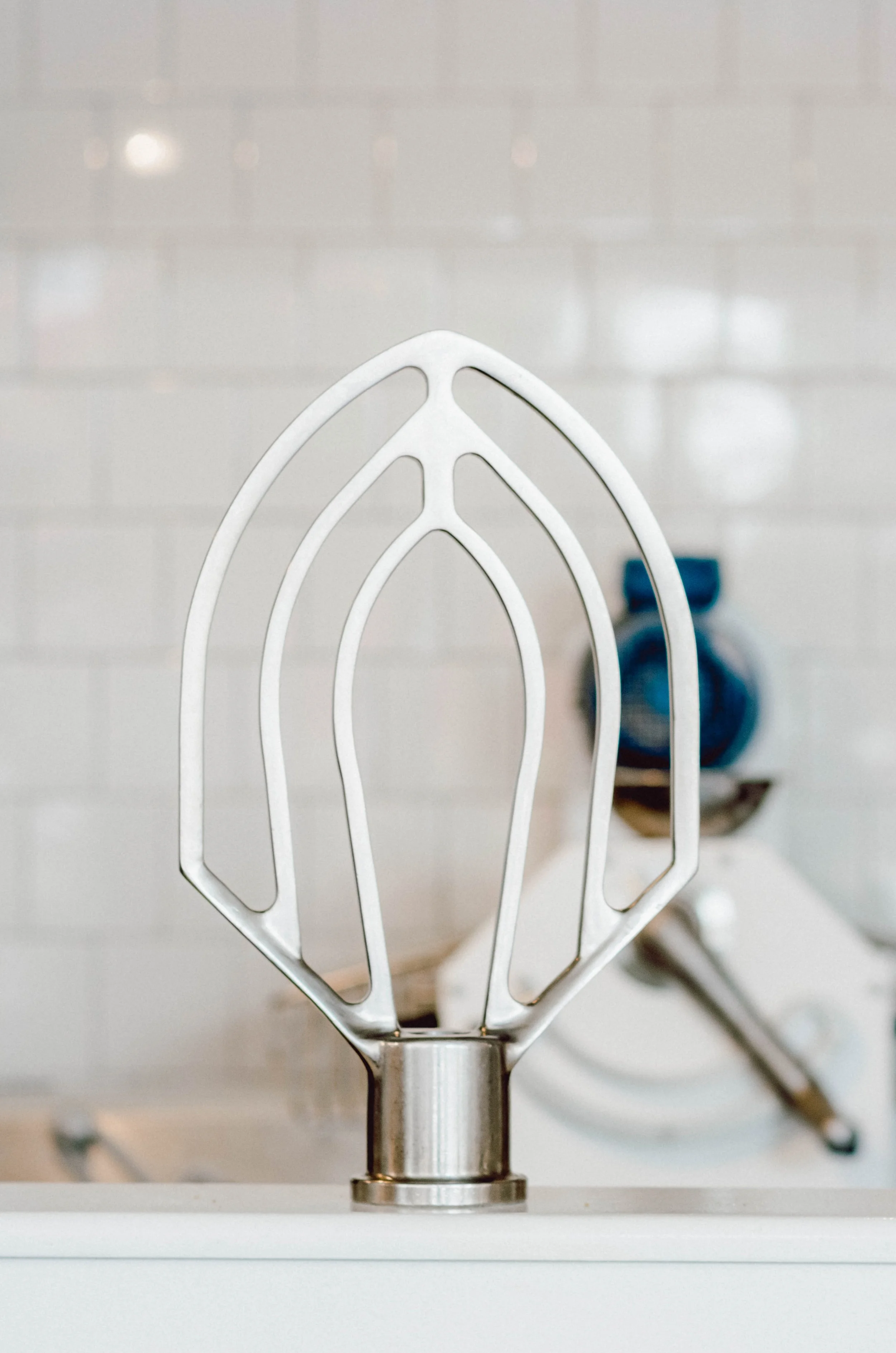 Close-up of a stand mixer attachment on a white countertop with a tiled wall background.
