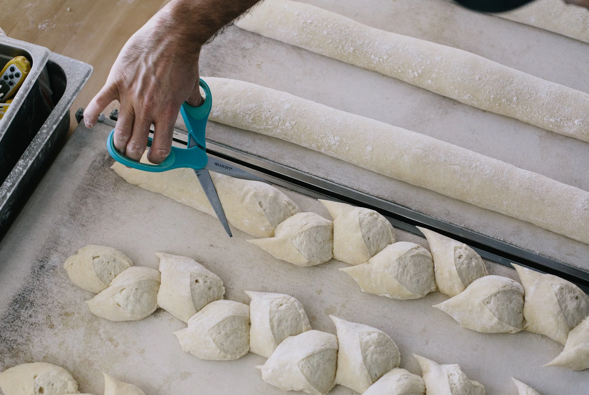 Person using scissors to cut shaped dough in a bakery.