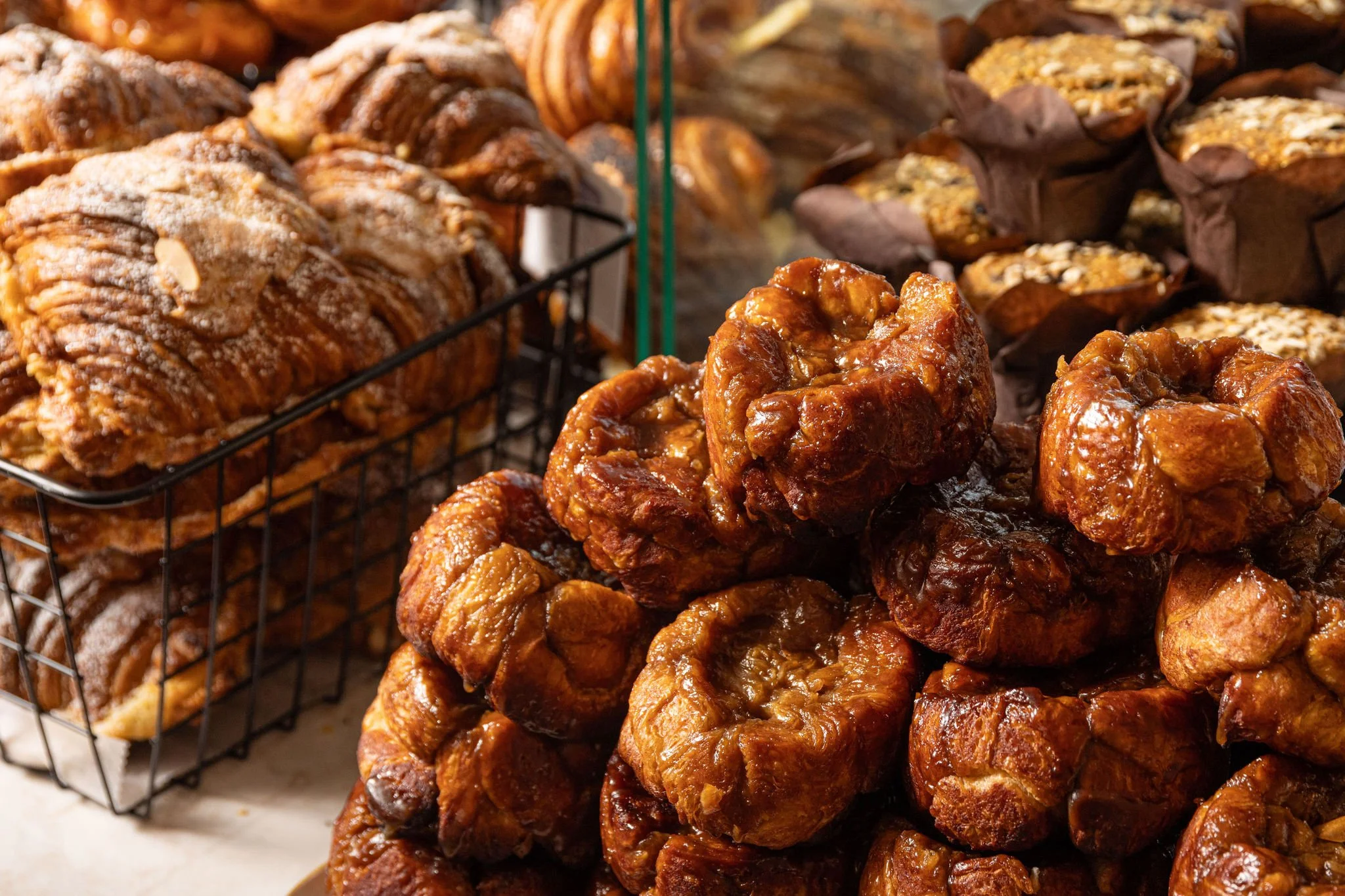 A display of baked goods, including large caramelized pastries, croissants, and muffins, on a bakery counter.