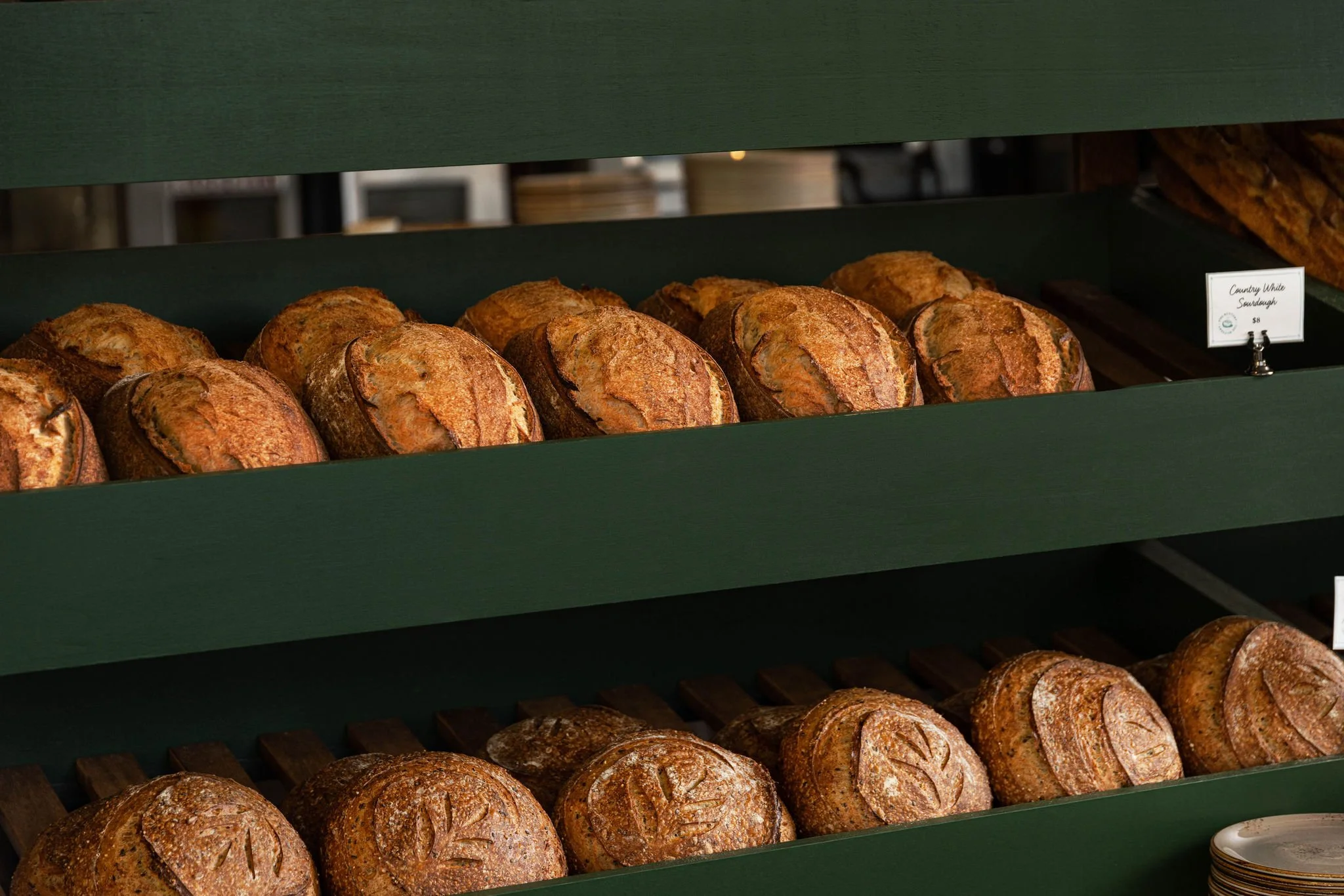 Multiple loaves of crusty bread on green display shelves in a bakery.