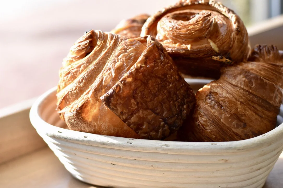 A white bowl filled with assorted croissants and pastries on a wooden surface.