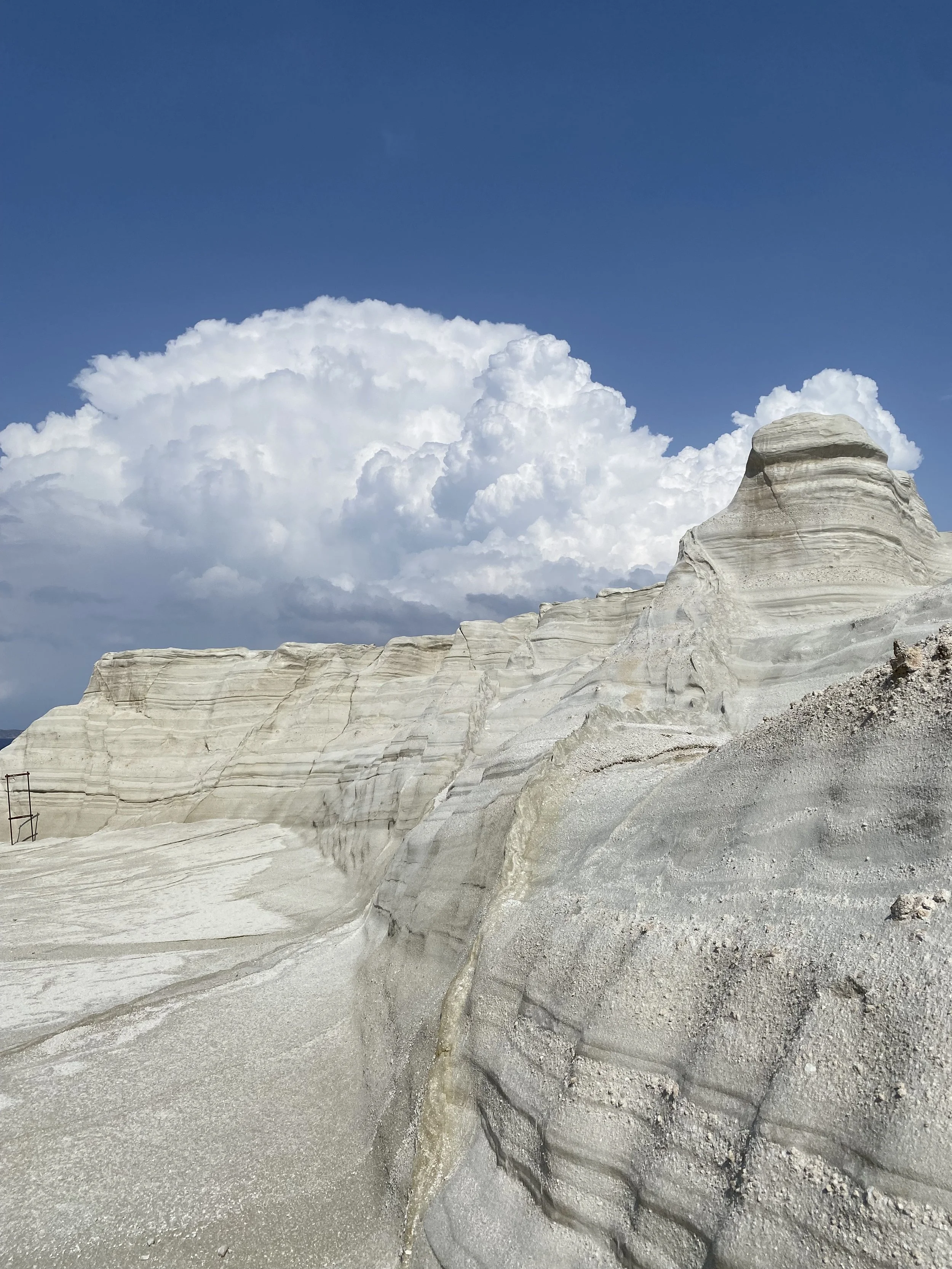 Formation géologique de roches blanches avec un ciel bleu et des nuages blancs déchiquetés en arrière-plan.