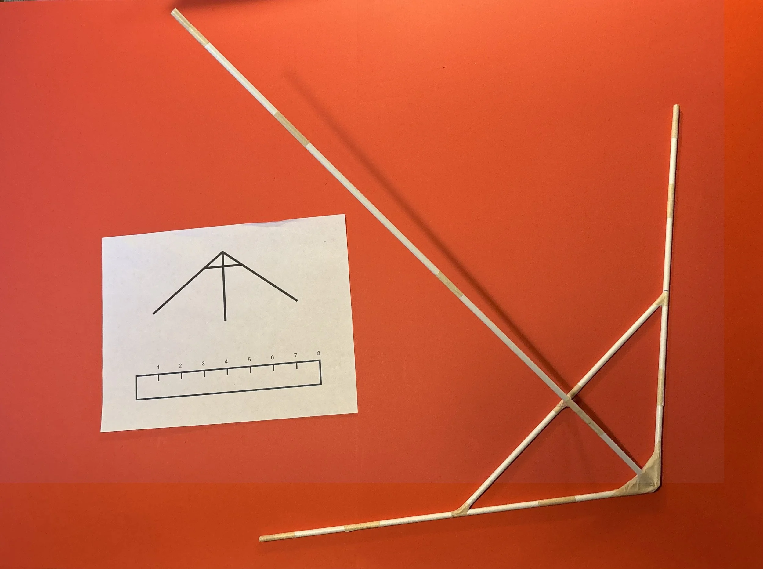 wooden kite frame on red background next to an instruction sheet with diagram