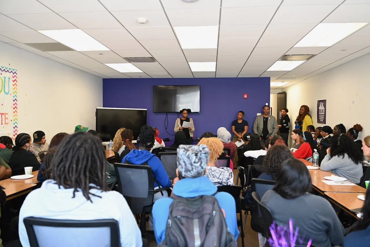 Group of people attending a presentation in a conference room with a woman speaking at the front.