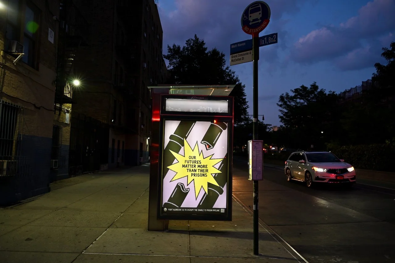 Bus stop advertisement with a graphic of explosions and bottles, with the text "Our futures matter more than their prisons" and smaller text at the bottom.