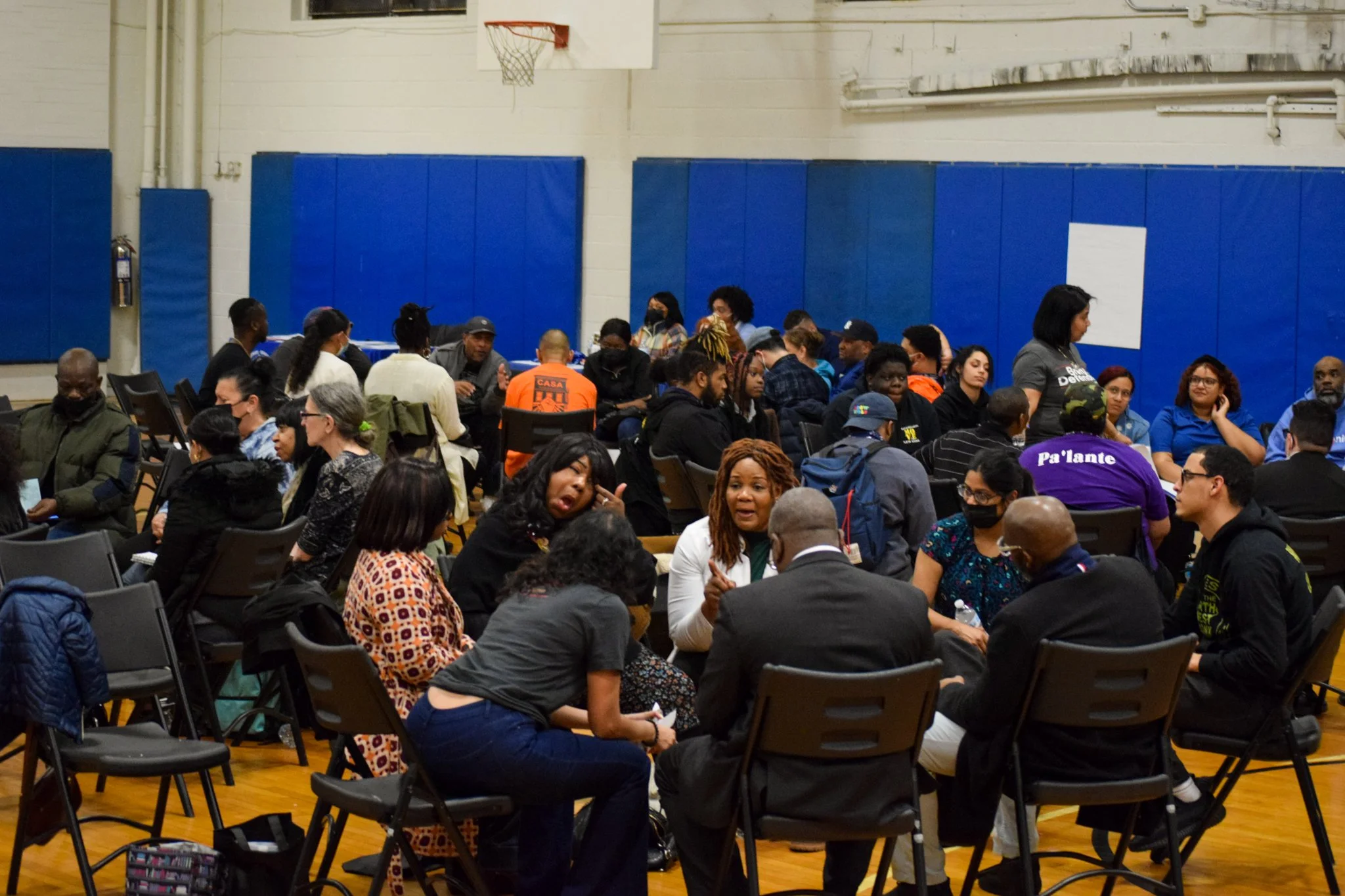 Group of diverse people seated in a gymnasium, engaged in conversation during a community event.