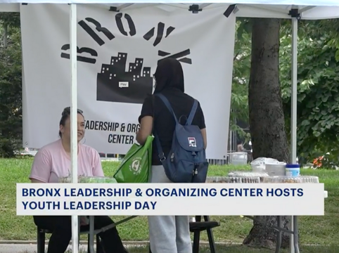 A person with a backpack talking to a woman at a booth under a white canopy tent. The booth banner reads 'Bronx Leadership & Organizing Center' and the caption mentions hosting Youth Leadership Day.