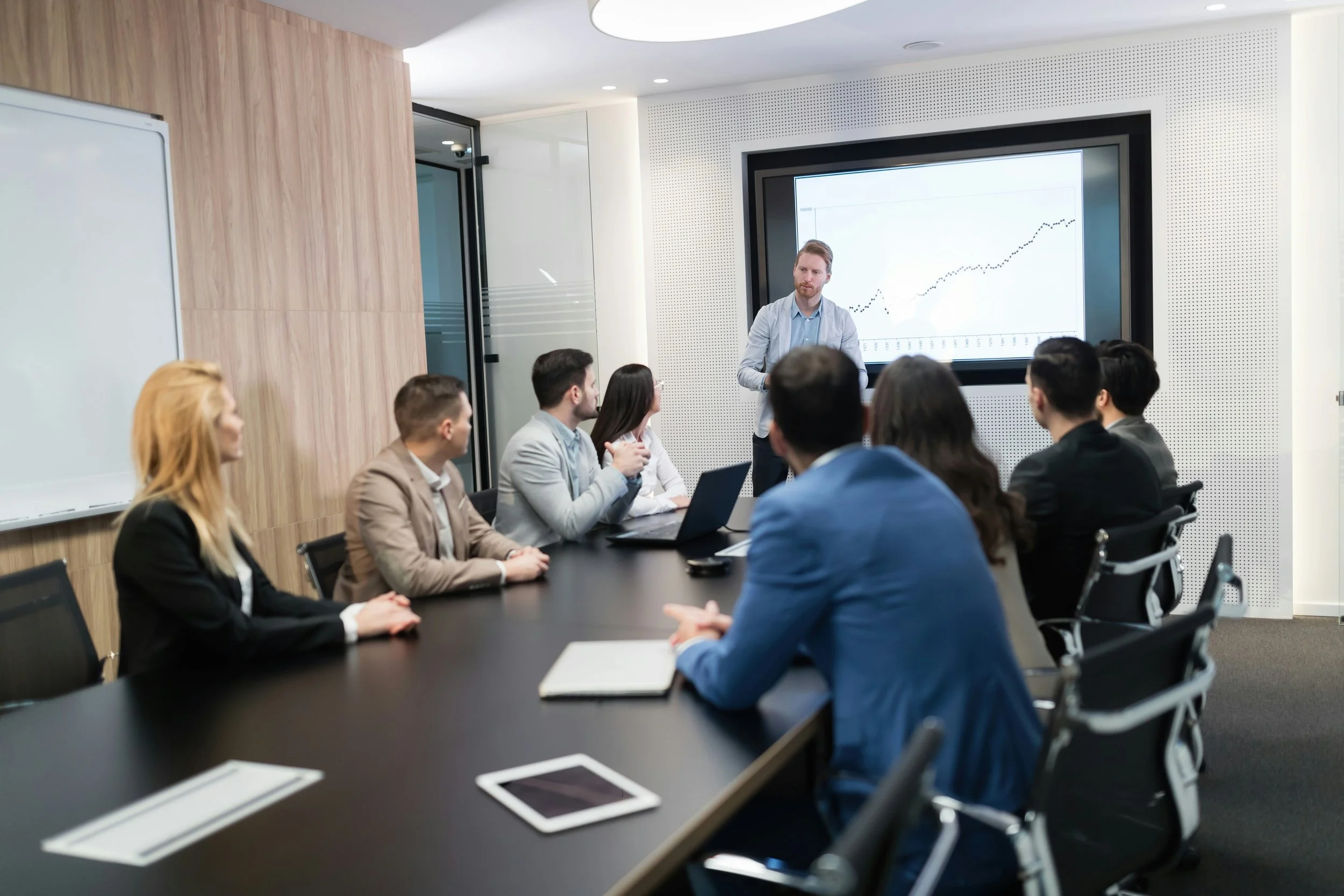 Business team in a boardroom presentation with leader showing financial growth chart on screen.
