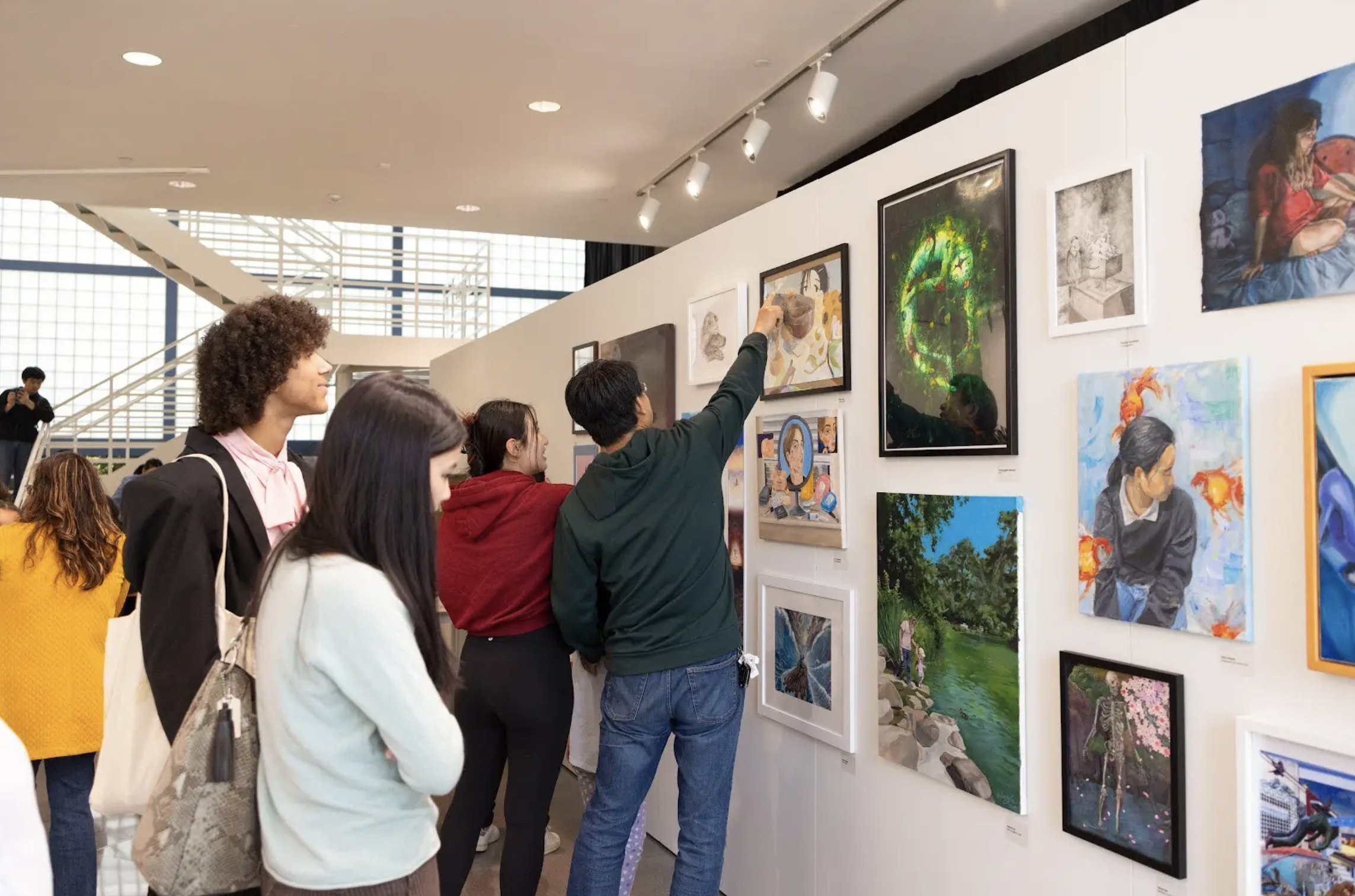 People viewing artwork in an art gallery, with several paintings displayed on the wall.