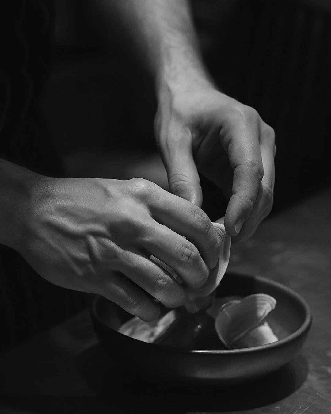 Close-up of hands opening a small container or jar over a dark dish.