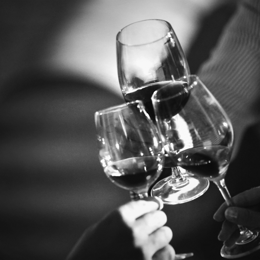 Four people clinking glasses of red wine in a toast, captured in black and white.